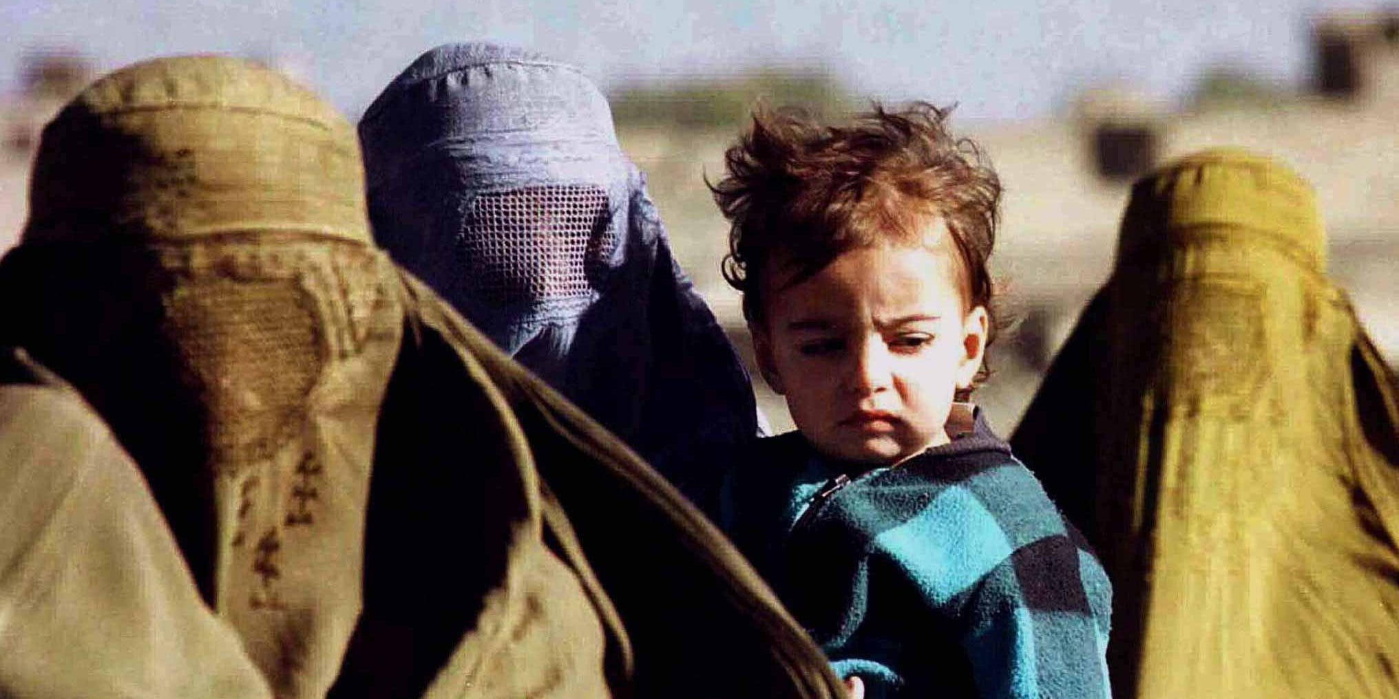 Women with covered bodies and faces hold a small child as they flee the Taliban in 1996