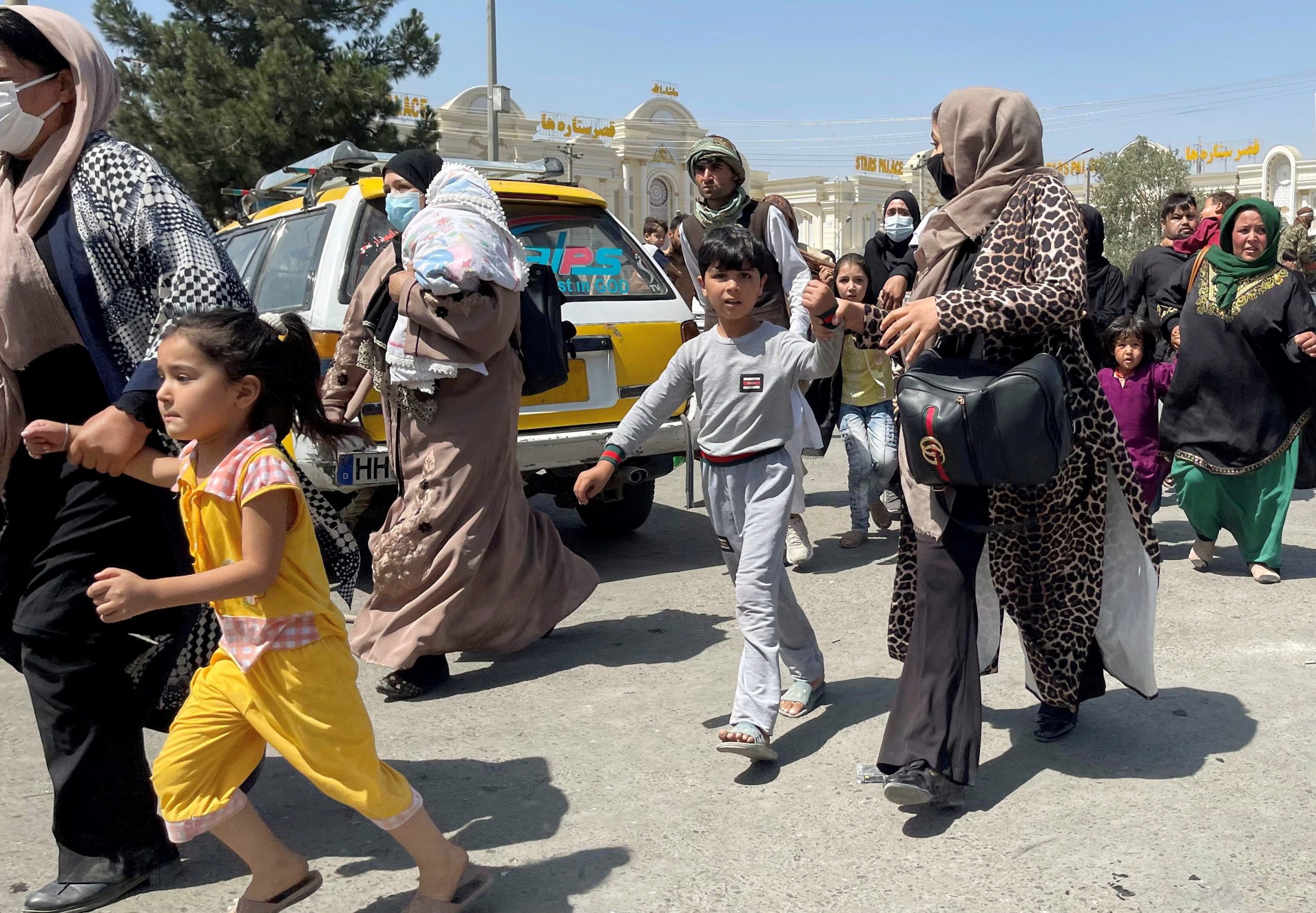 Women hold hands with their children as they run across a street