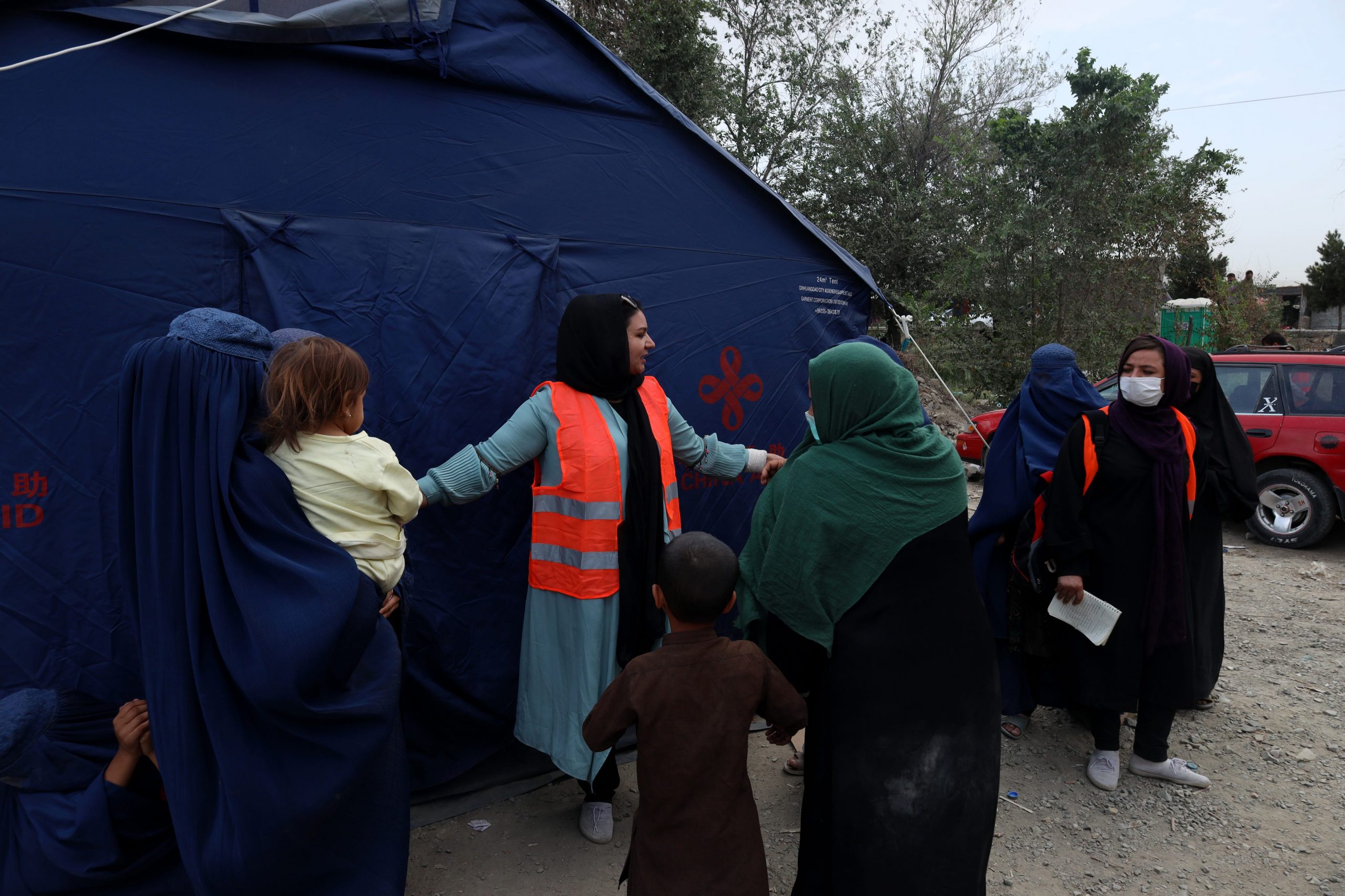 a woman in an orange vest speaks to other women in kabul