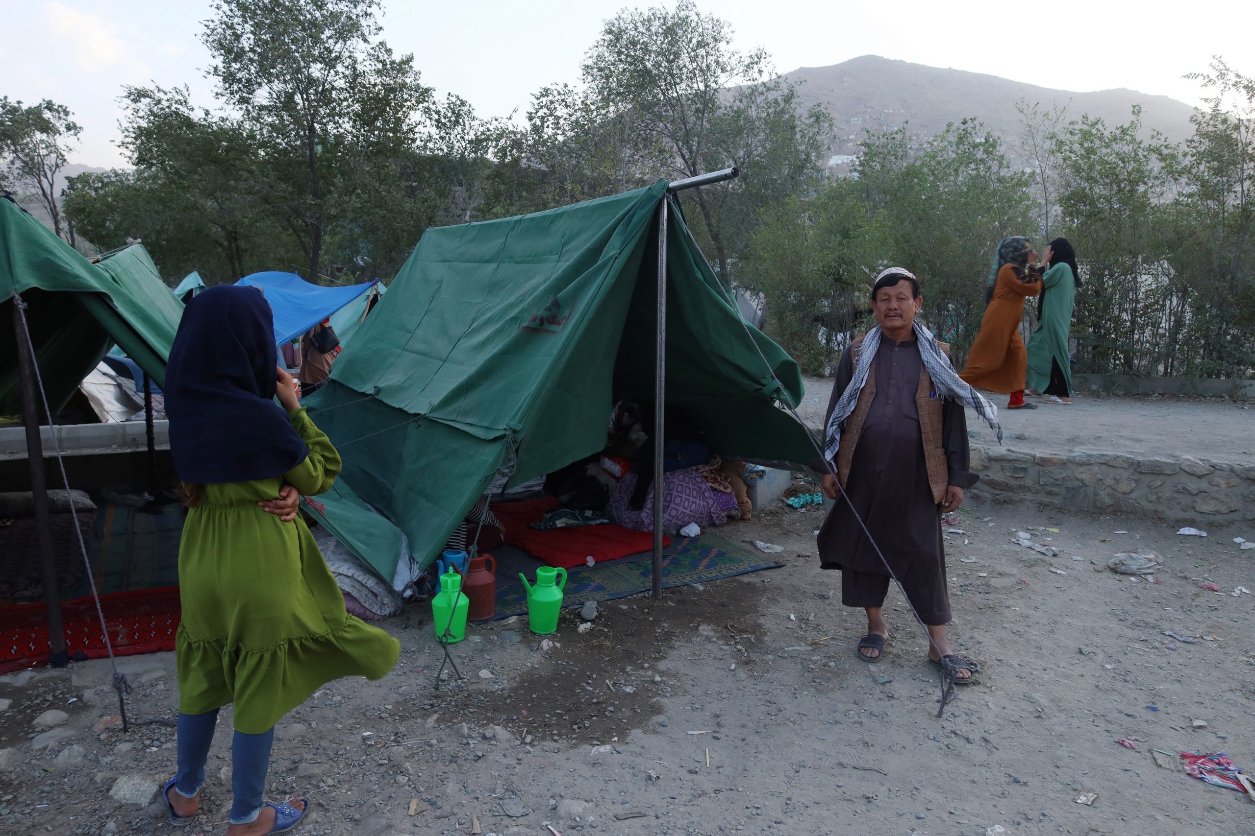 a man stands outside a green tent at a makeshift refugee camp in kabul