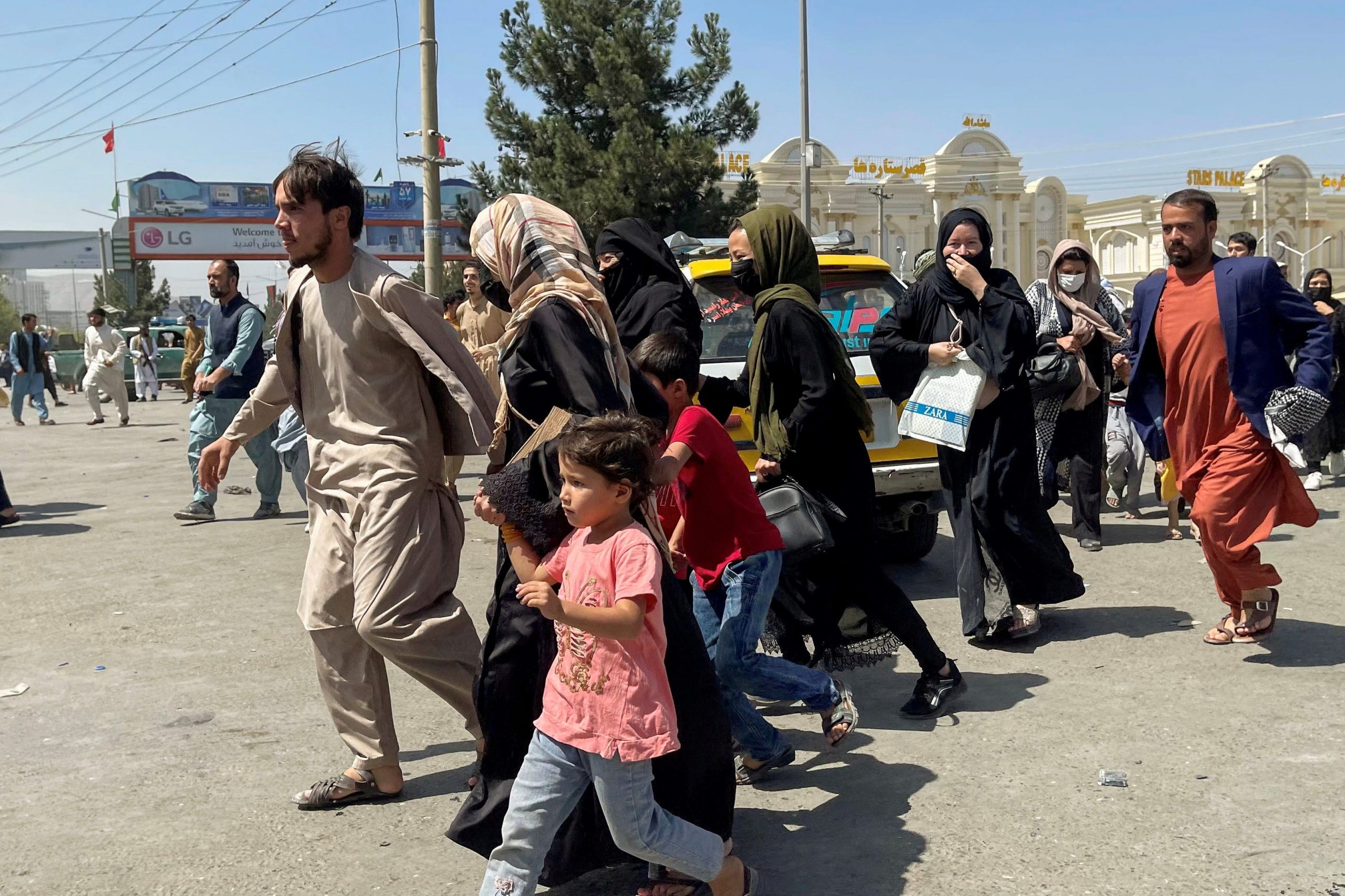 A dozen Afghan people are running, one woman is holding the hand of a child.