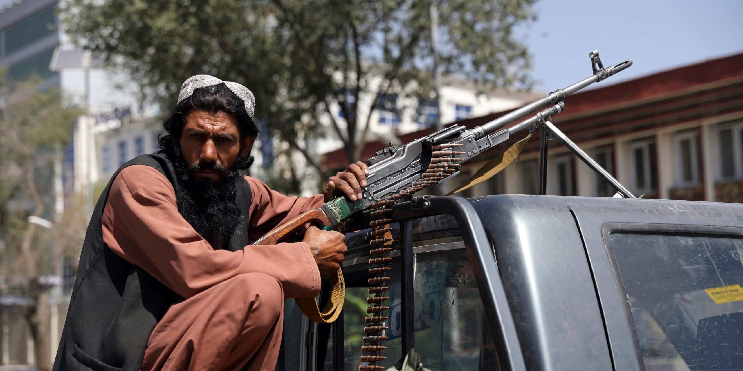 A Taliban fighter sits in the back of a truck holding a machine gun.