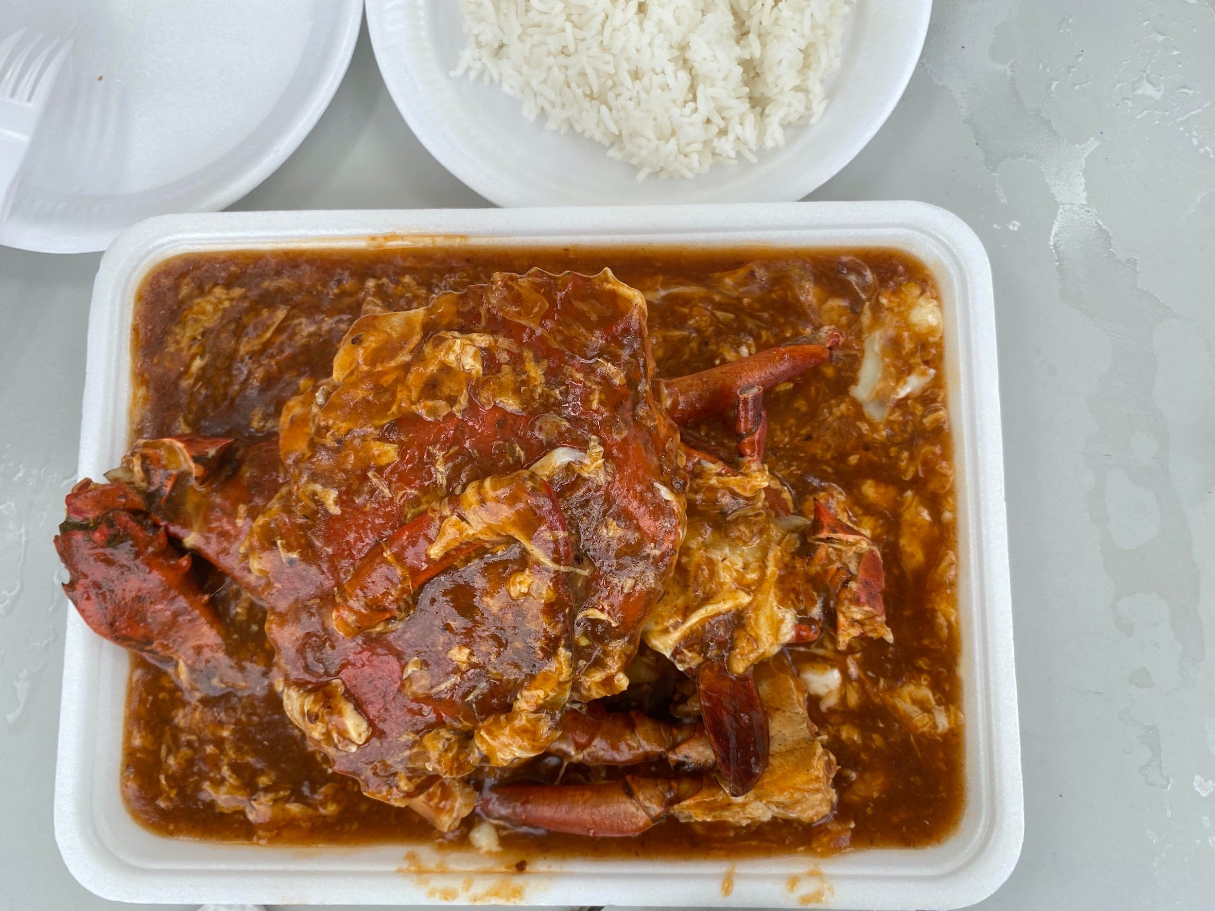 a paper plate of chili crab with white rice at a hawker center in singapore