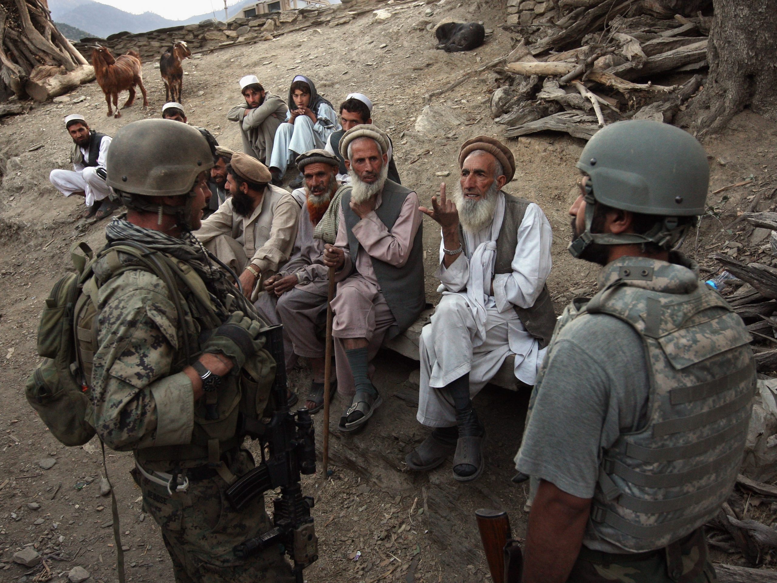 An Afghan man, wearing white, speaks to a crowd of US soldiers