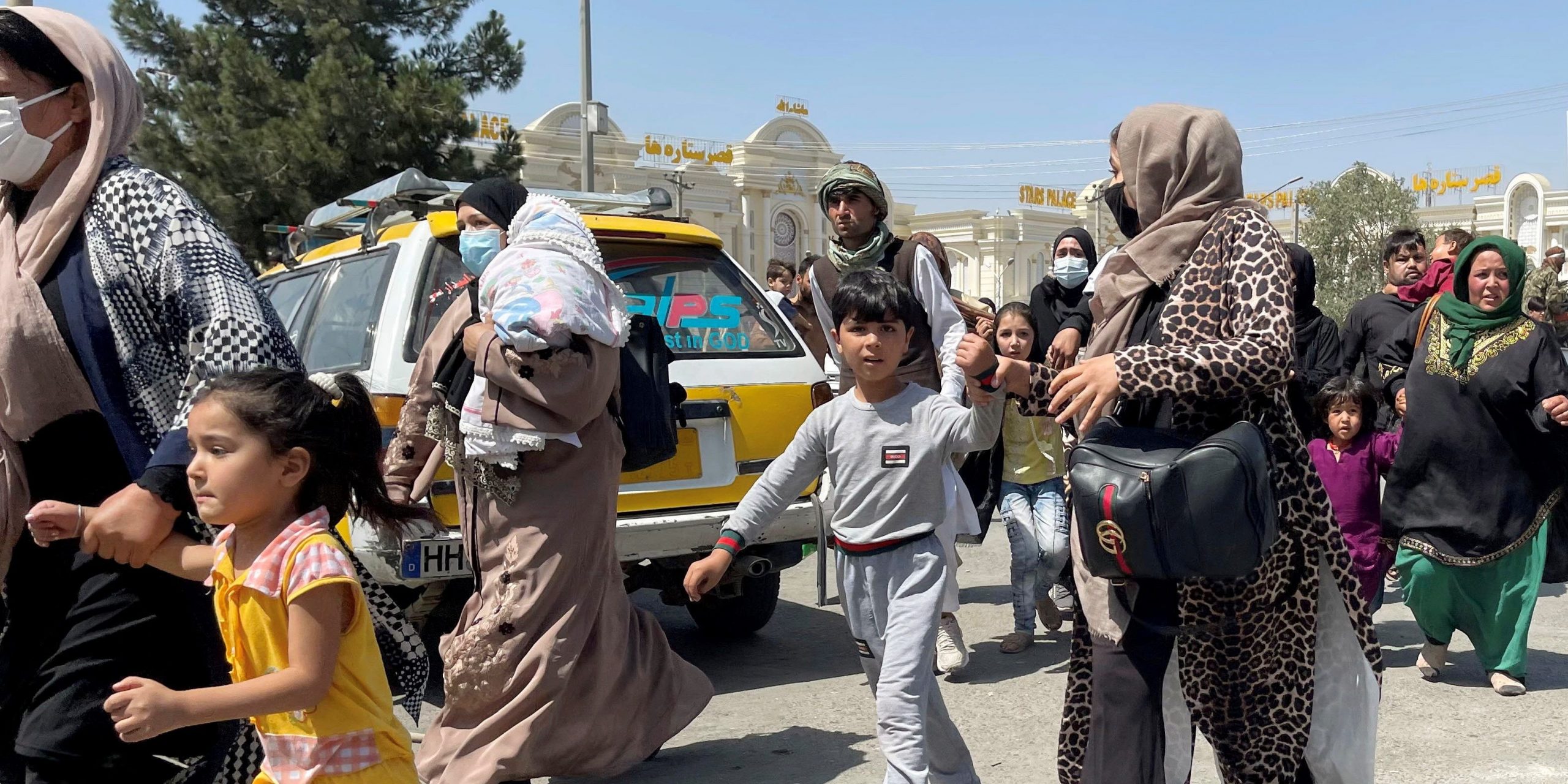 Women hold hands with their children as they run across a street