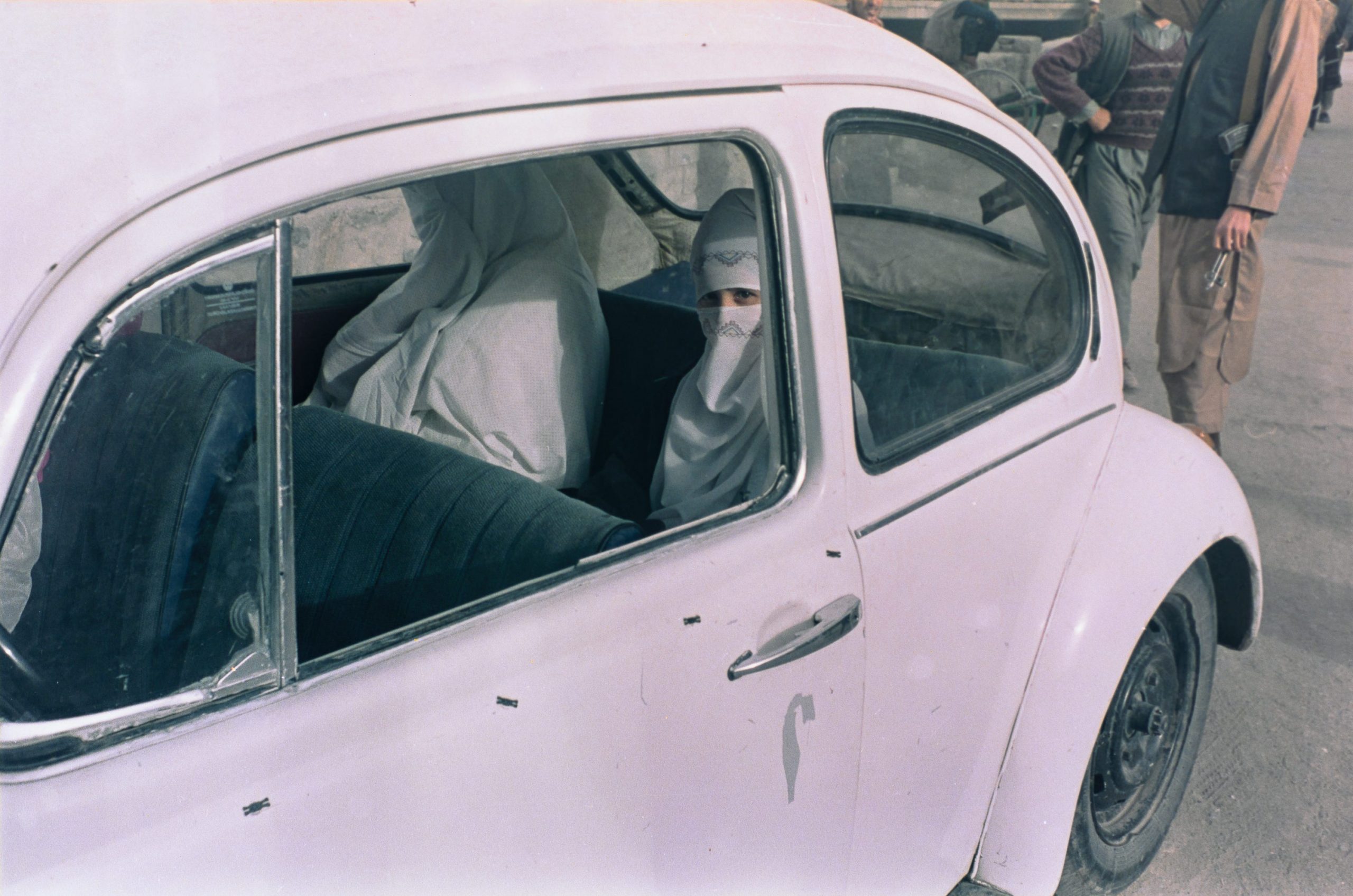 Two women, fully veiled, are seen in the back of a car.