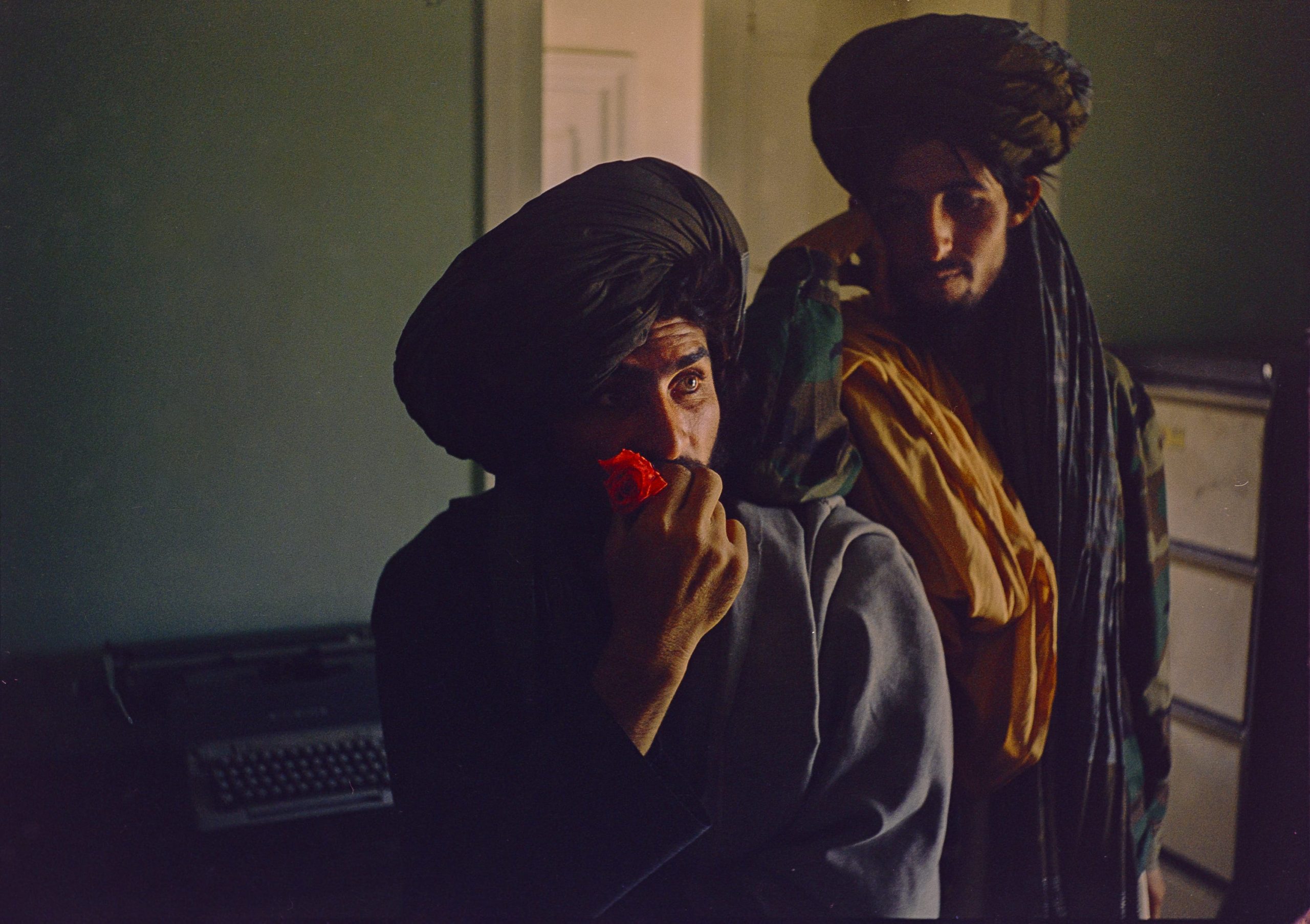 A Taliban fighter holds a flower in his hand, as another stands behind him.