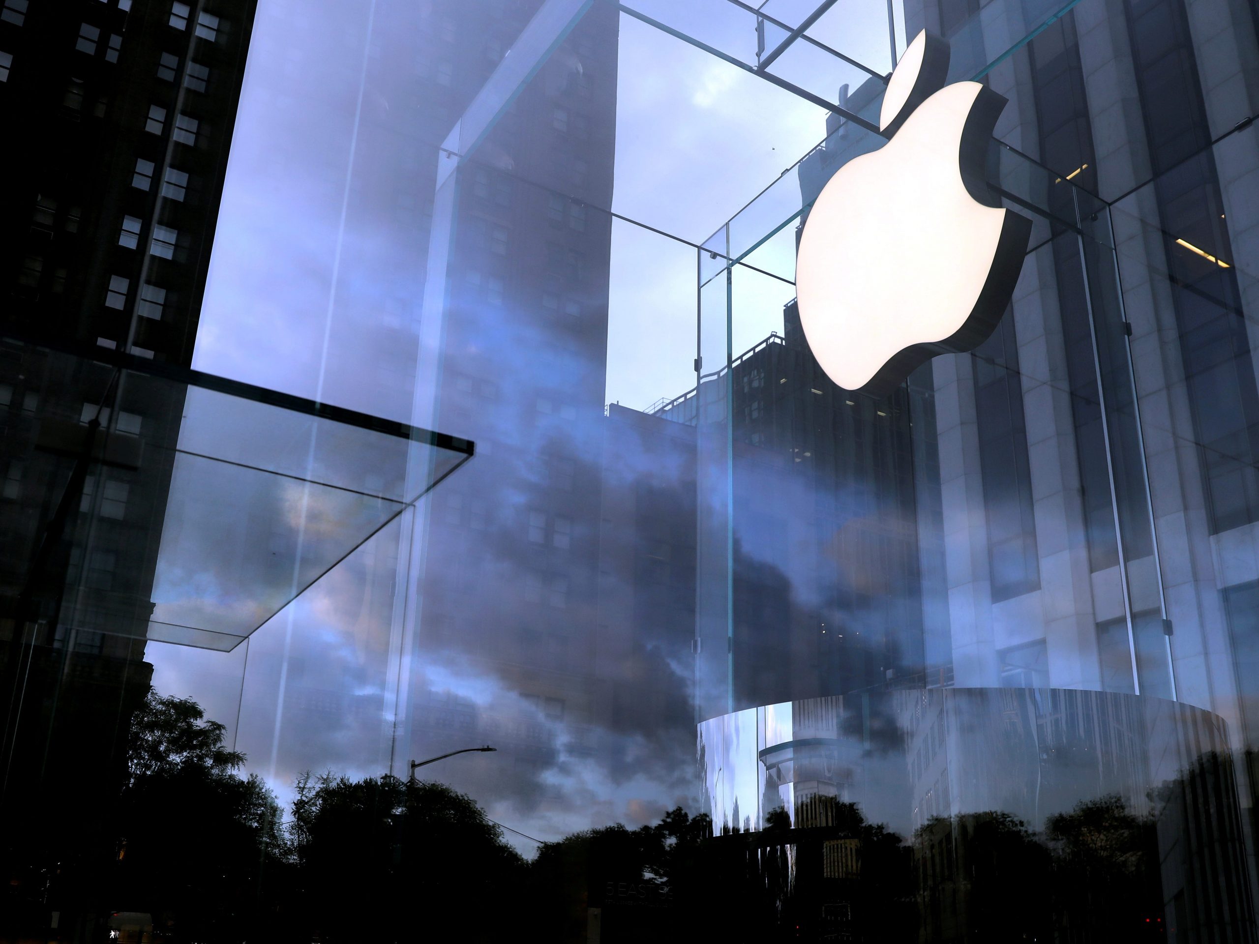 A cloudy sky behind a brightly lit Apple logo in a Manhattan store