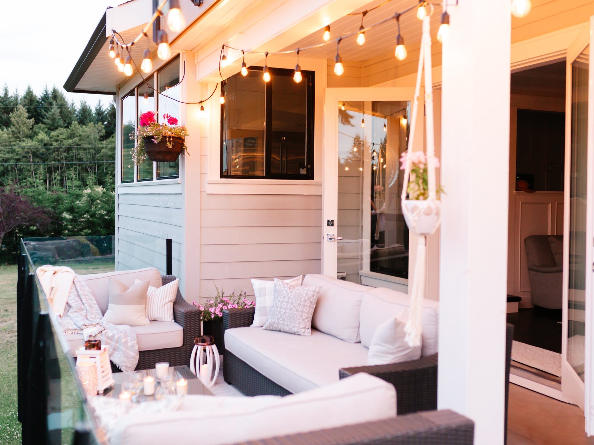 A front porch decorated with white couches and chairs and string lights