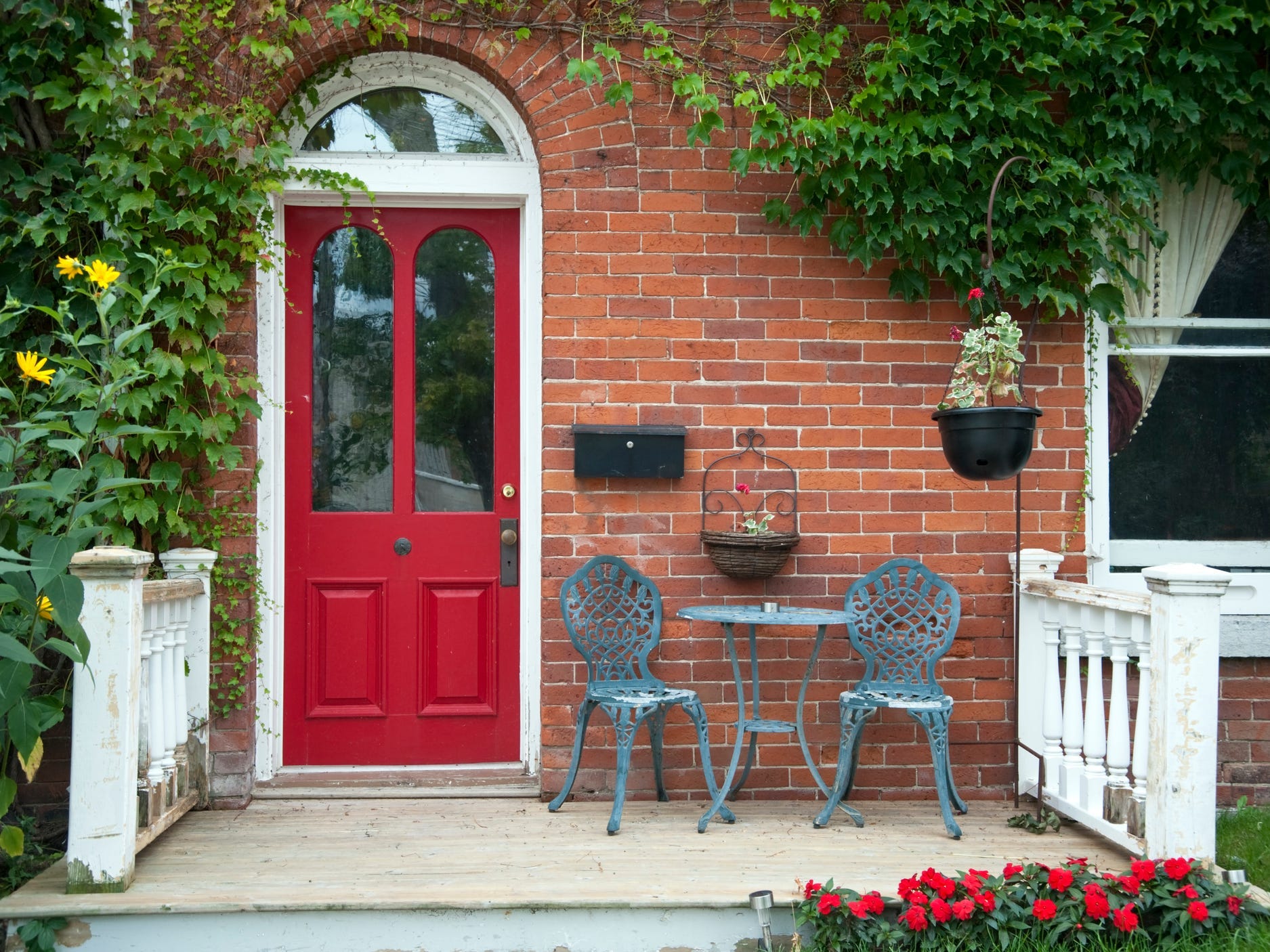 The front porch of a brick house with a red door and lush ivy