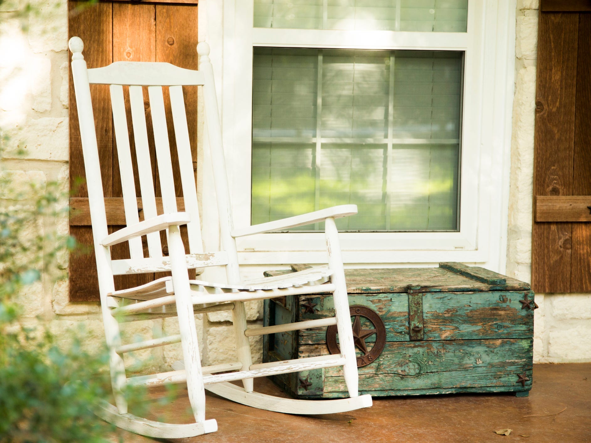 A front porch with a white rocking chair and rustic blue trunk