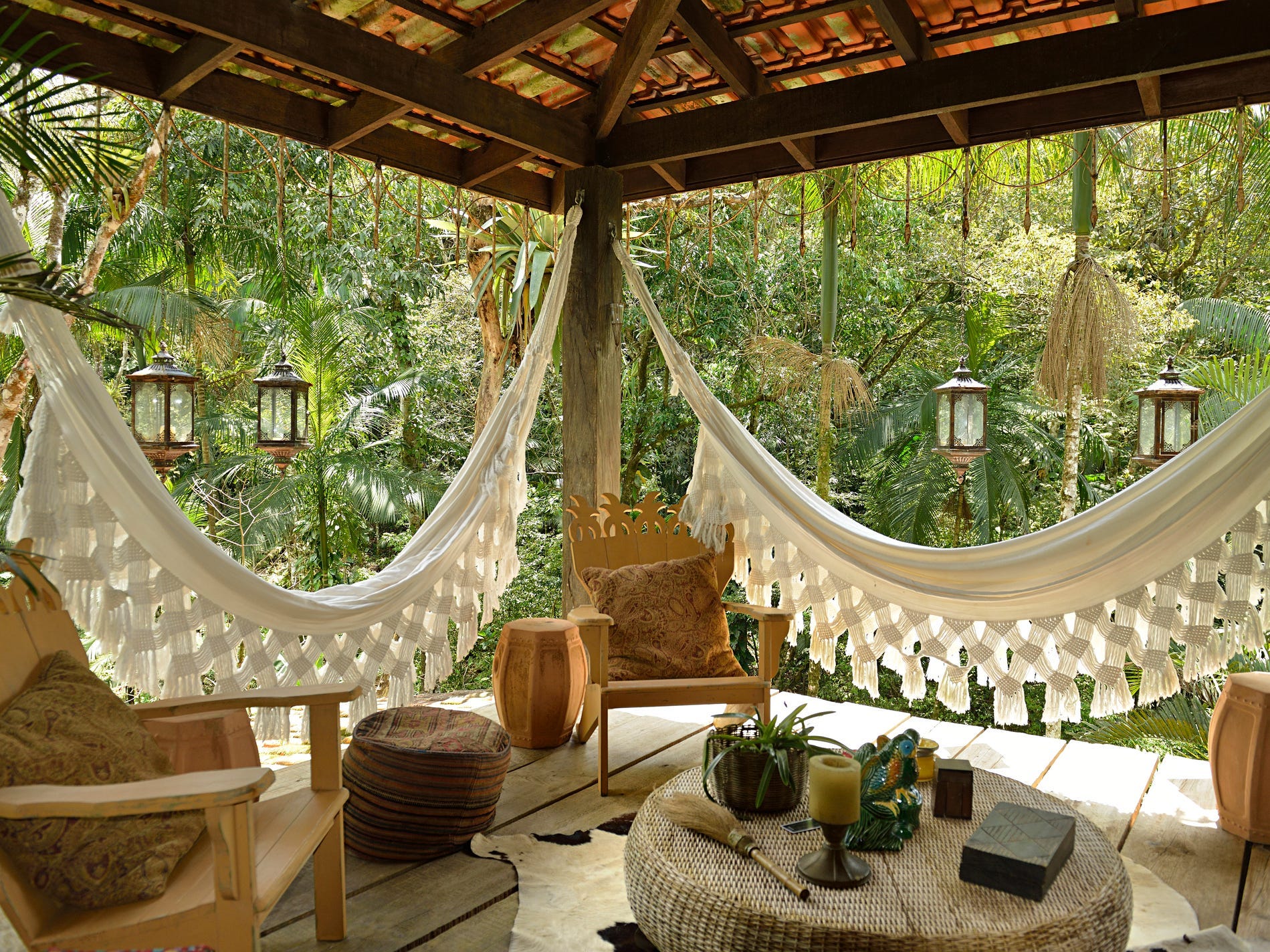 A porch in a lush tropical landscape decorated with wooden chairs and macrame hangings