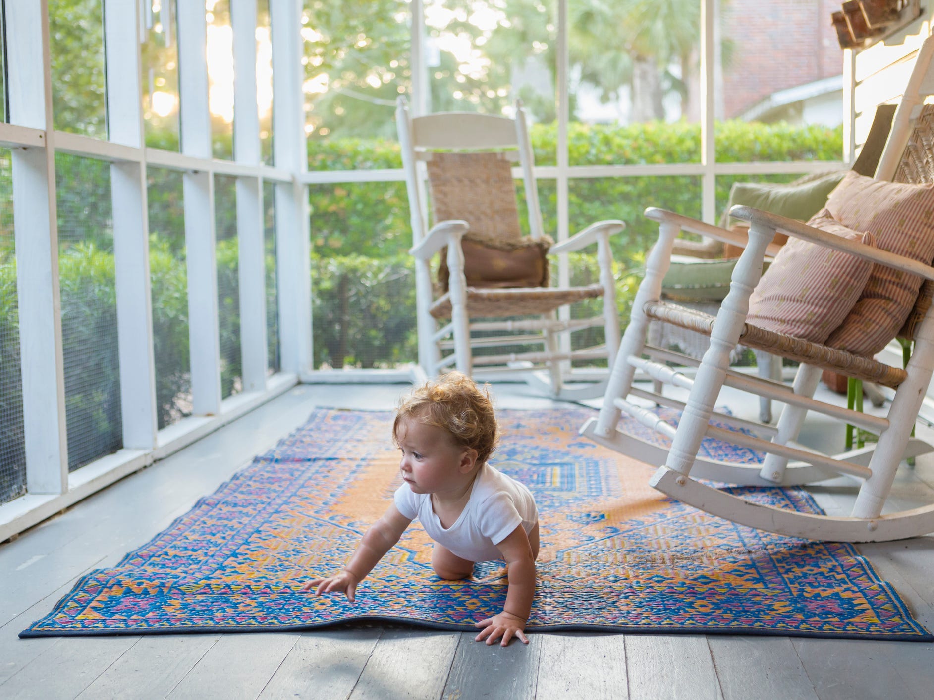 A baby crawling on a rug on a porch with two rocking chairs in the background