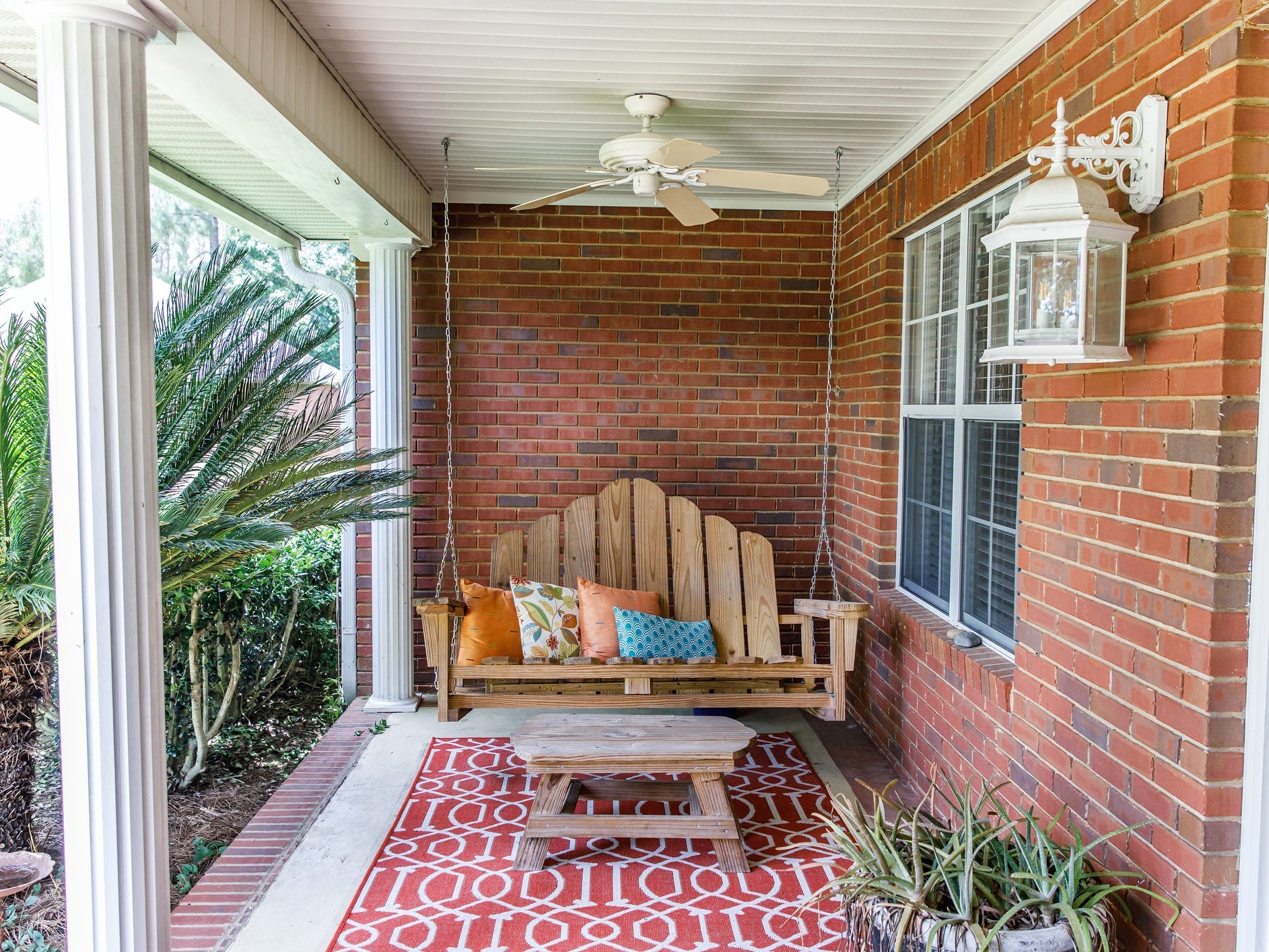 A wooden porch swing hanging on the porch of a brick house