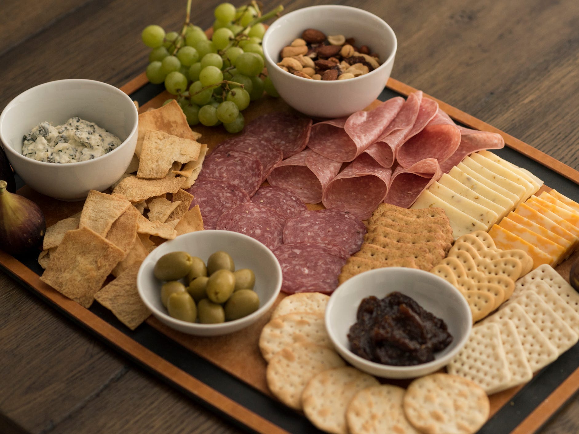 A charcuterie board with crackers, meats, and bowls of spreads and olives.