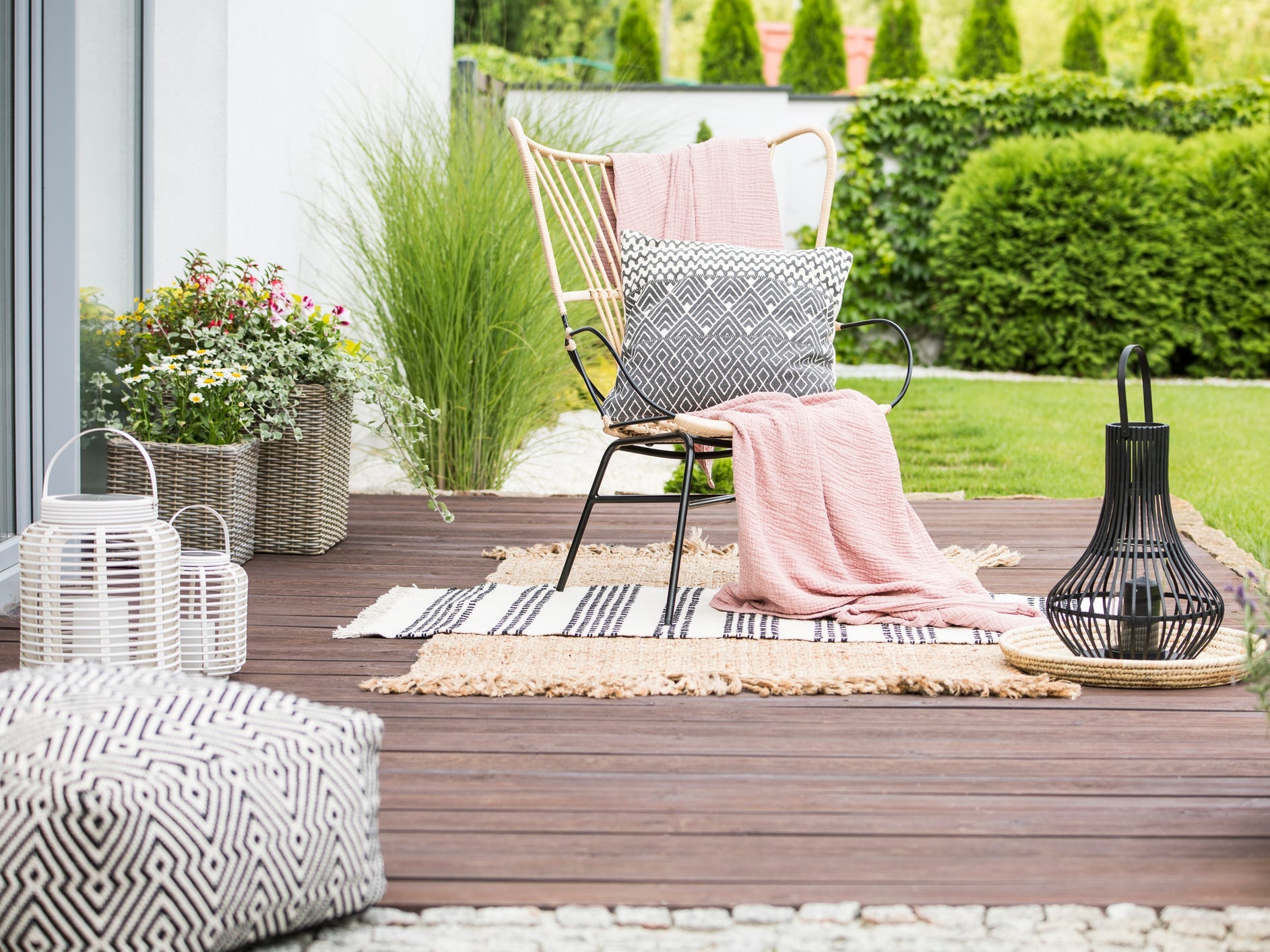 A patio decorated with a wire chair draped in blankets and pillows and sitting on two area rugs