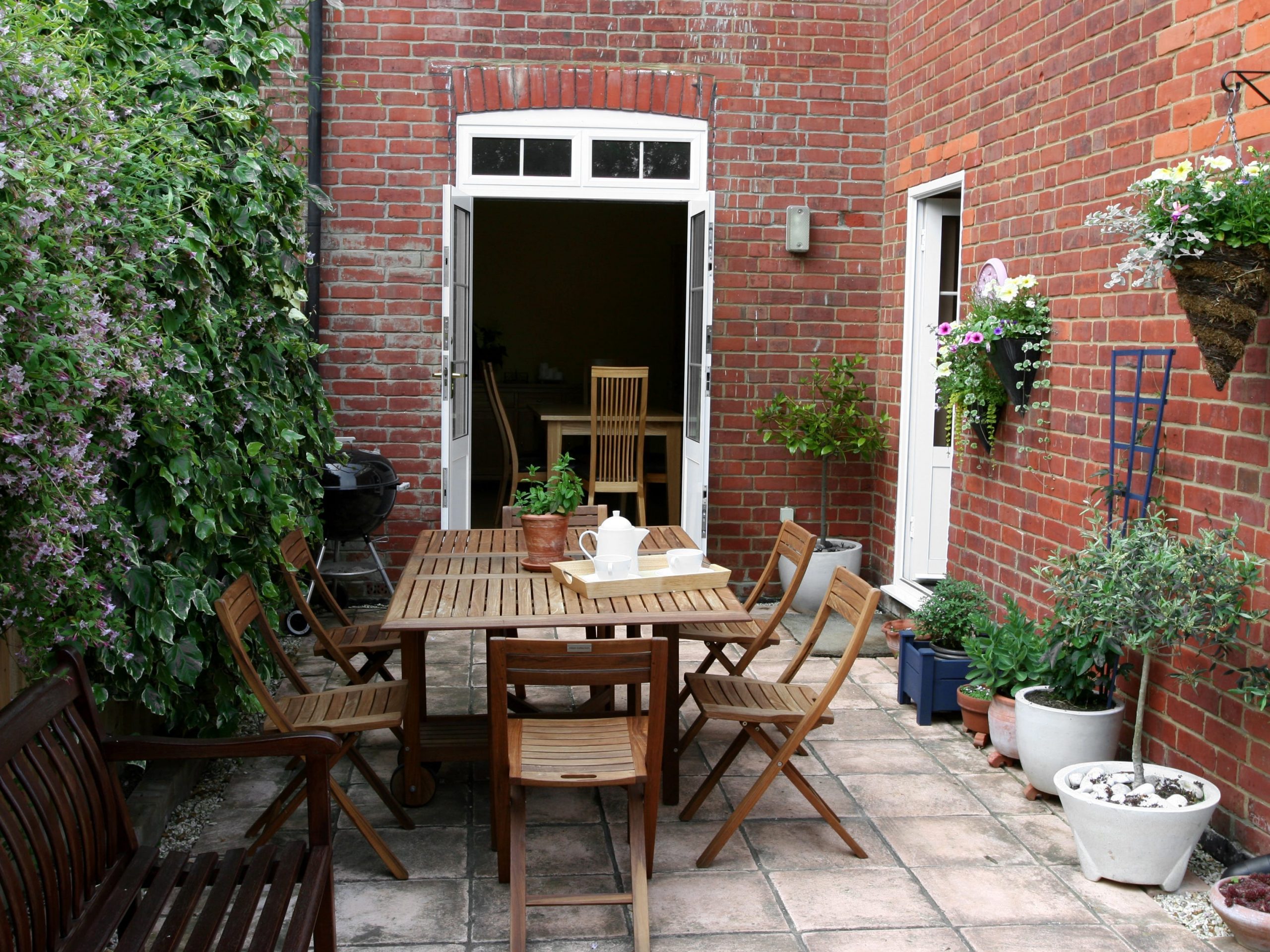 The patio fo a brick house decorated with dining furniture and closed off by a wall of plants