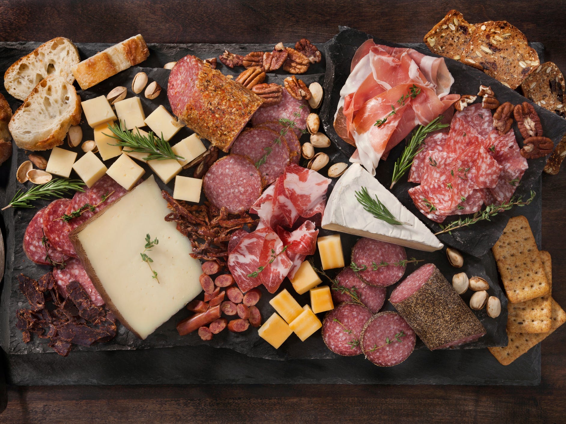 Charcuterie board with meats, cheeses, nuts, breads, and crackers.