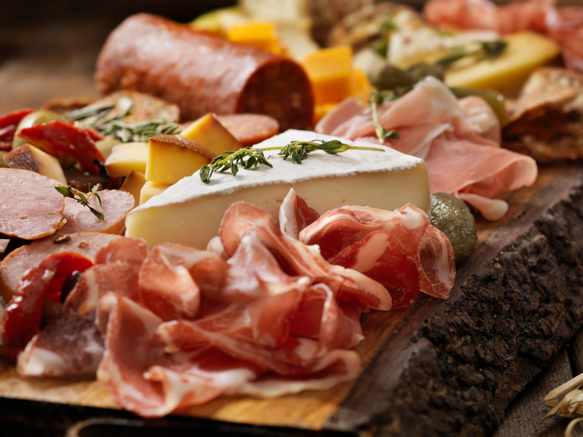 Meats folded in front of a block of cheese on a charcuterie board.