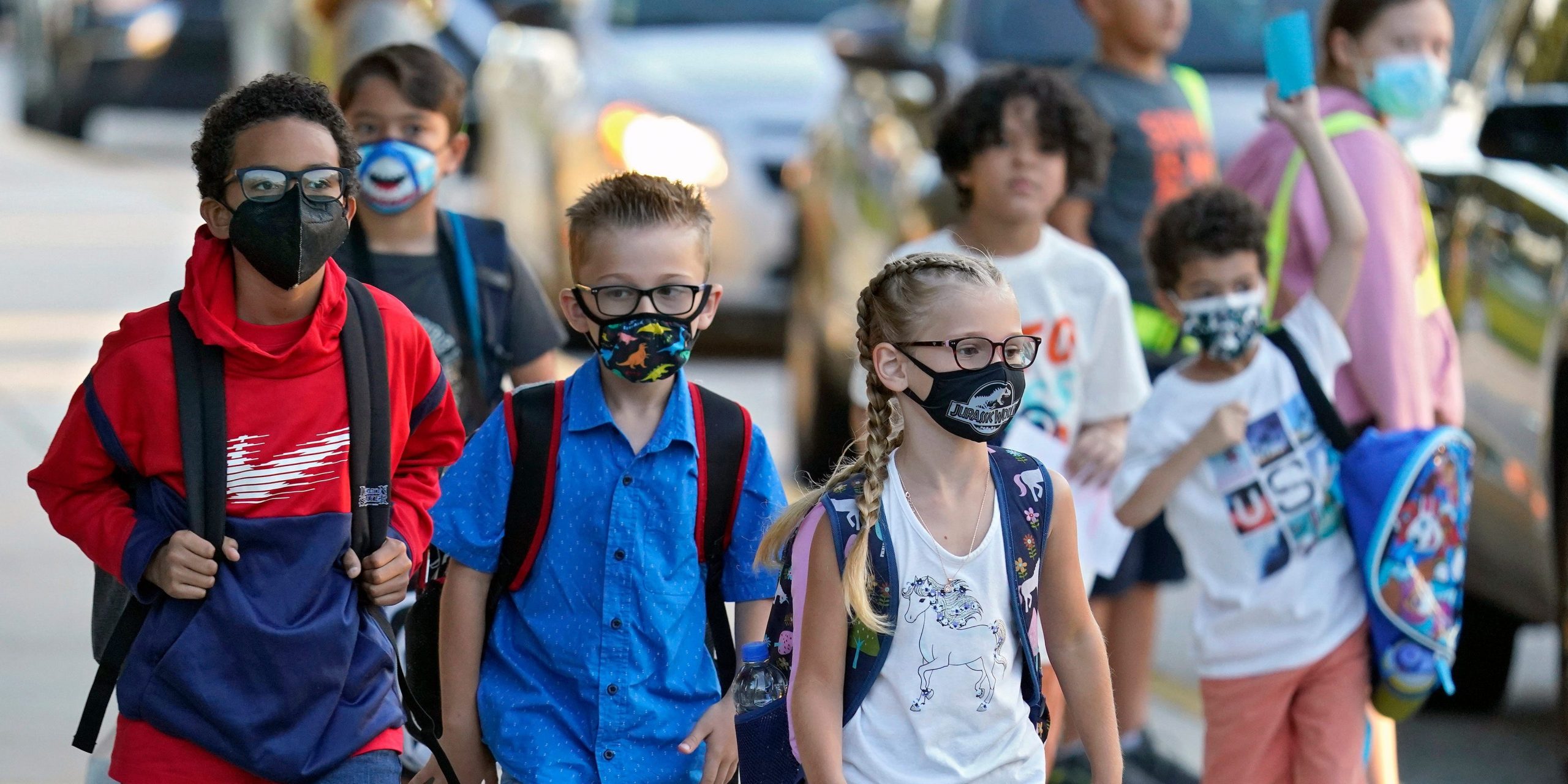 School children walk with masks and backpacks on.