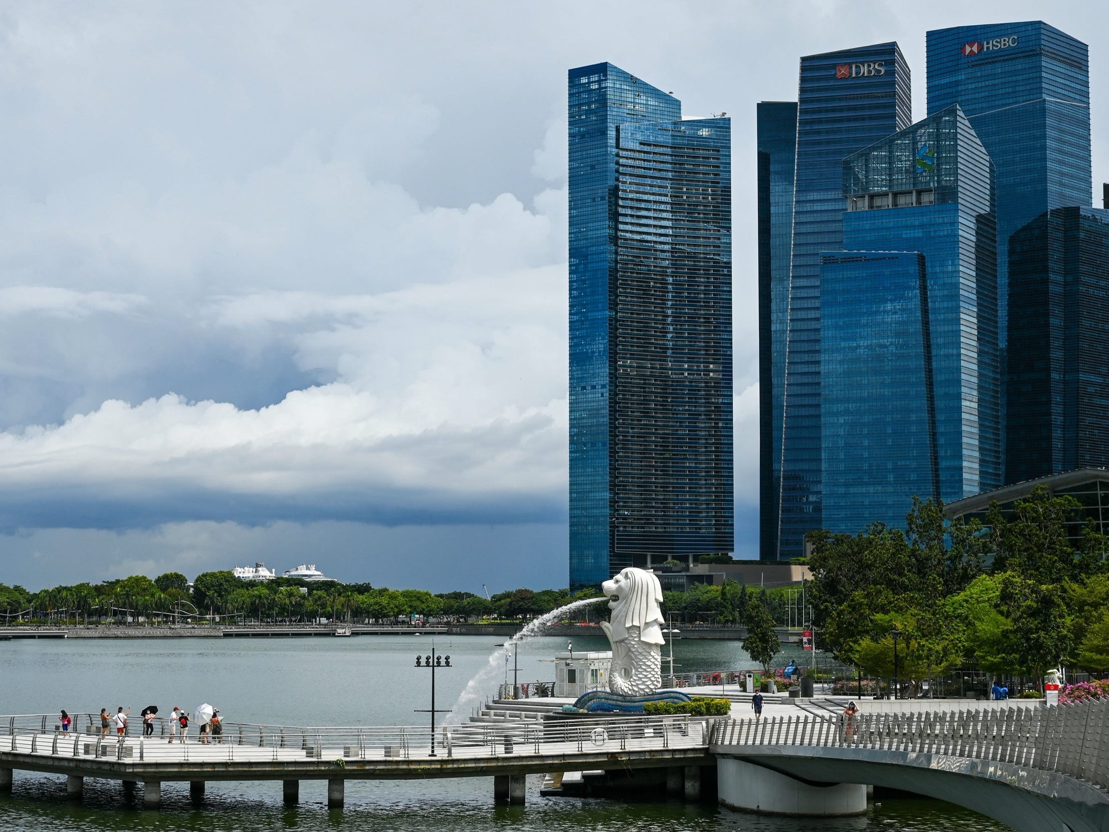 People stand along a pier next to a Merlion statue with skyscrapers in the background in Singapore