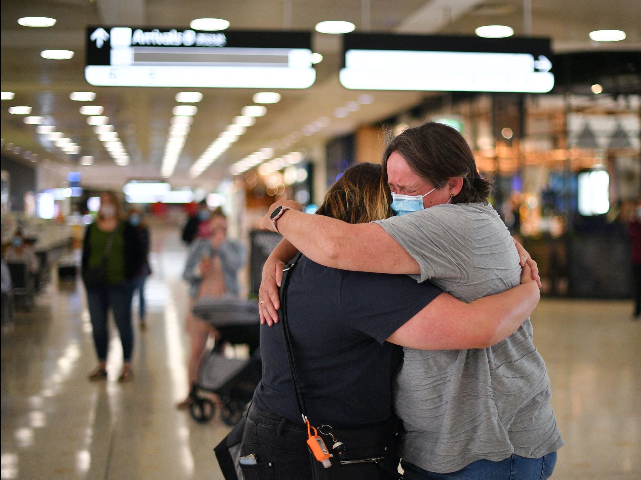 a masked mother and daughter hug in an airport