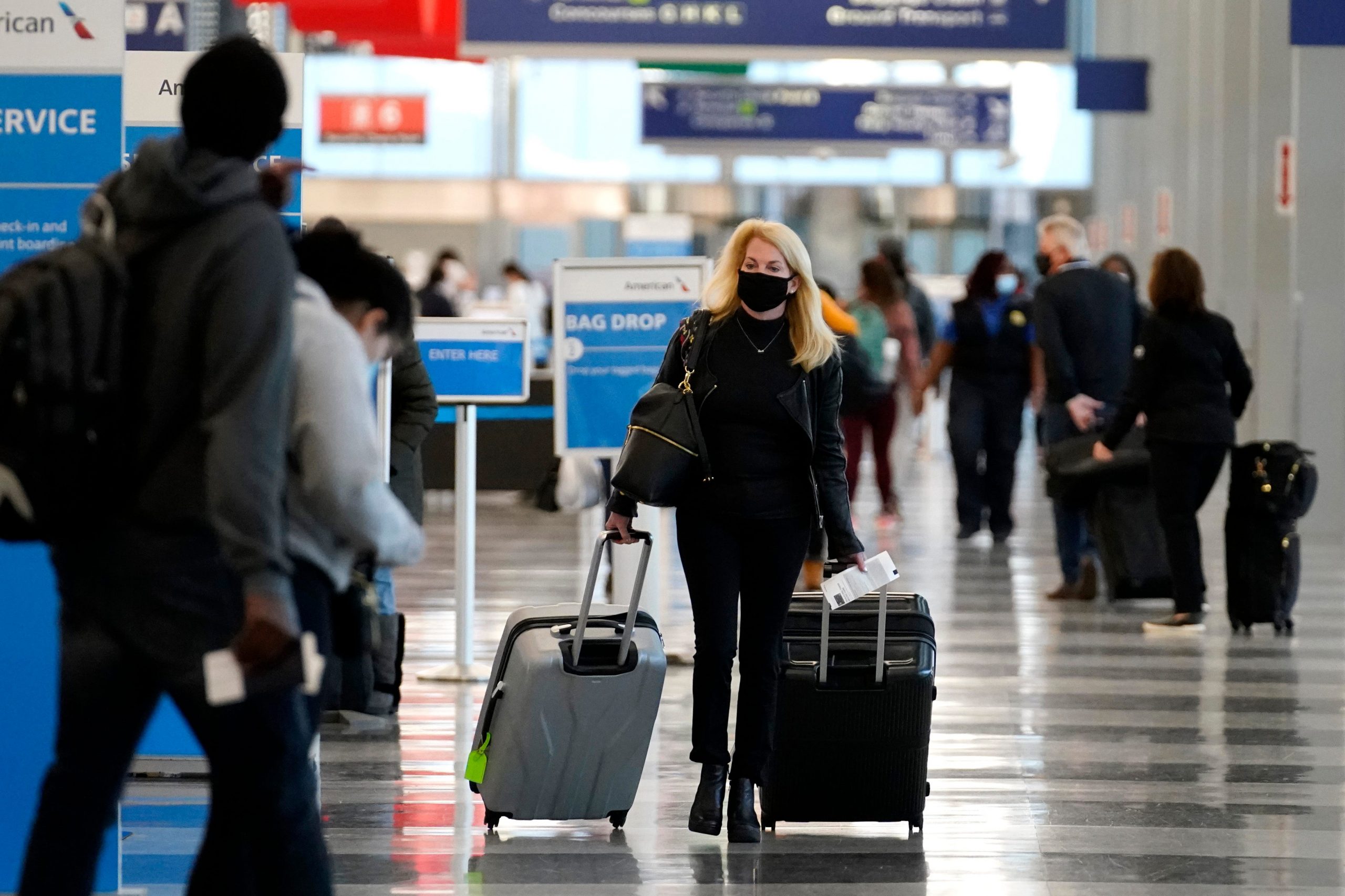 A woman in a mask pulls two suitcases through an airport terminal
