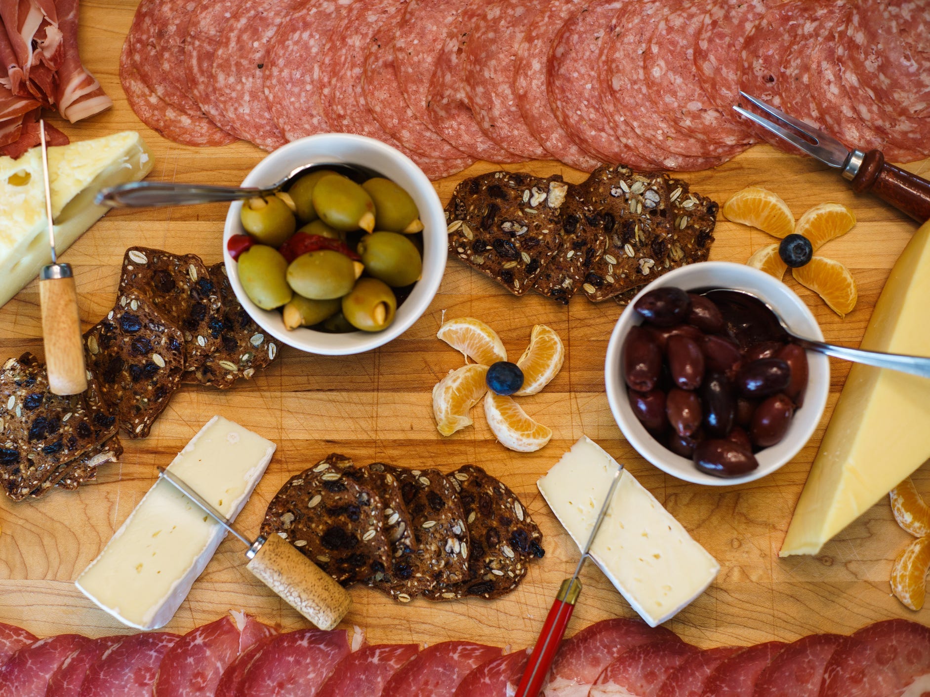 Charcuterie board with cheese, meats, oranges, blueberries, and olives.