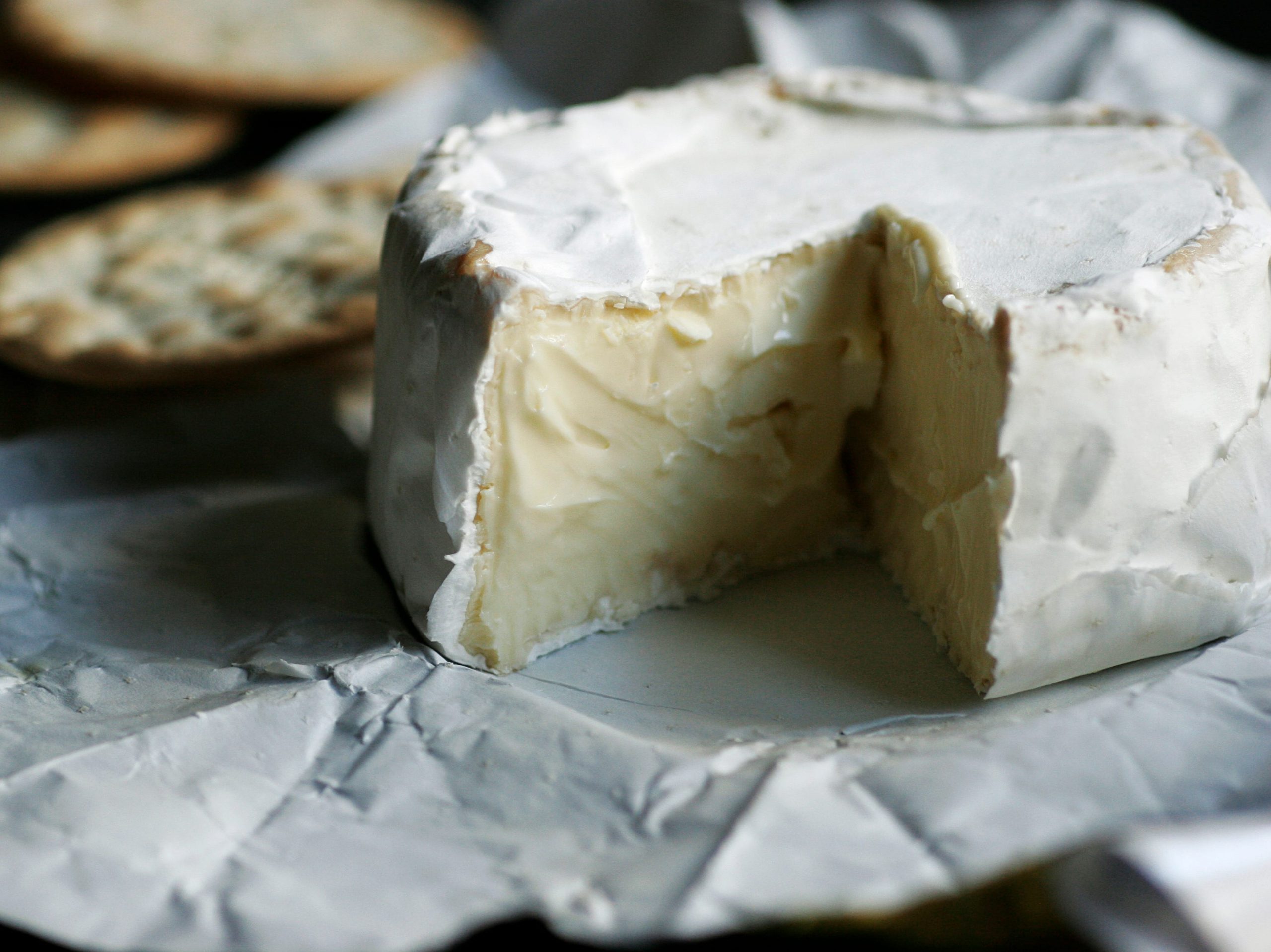 A round of brie with some crackers in the background.