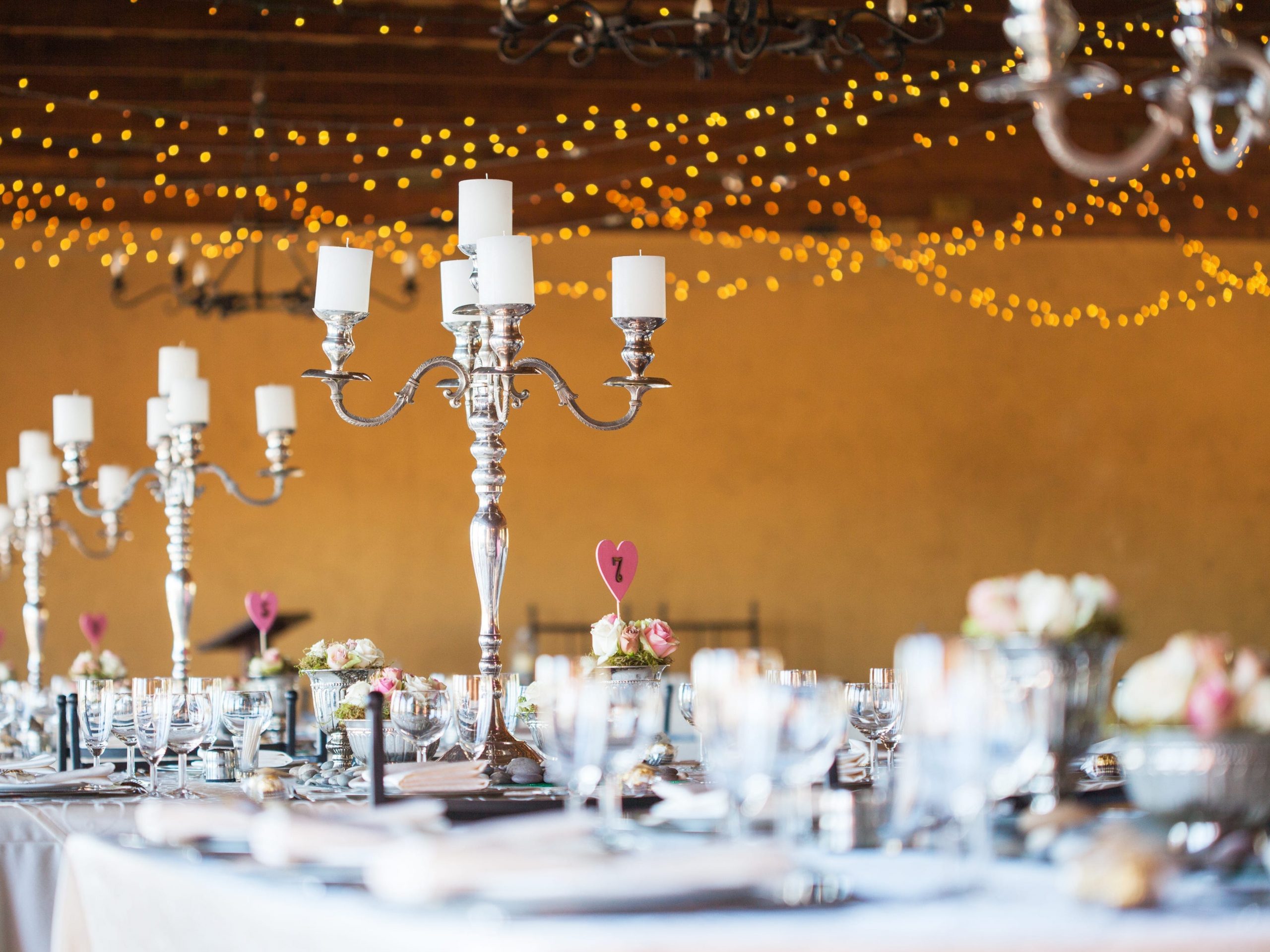 wedding venue table with candelabras and place settings, fairy lights in background