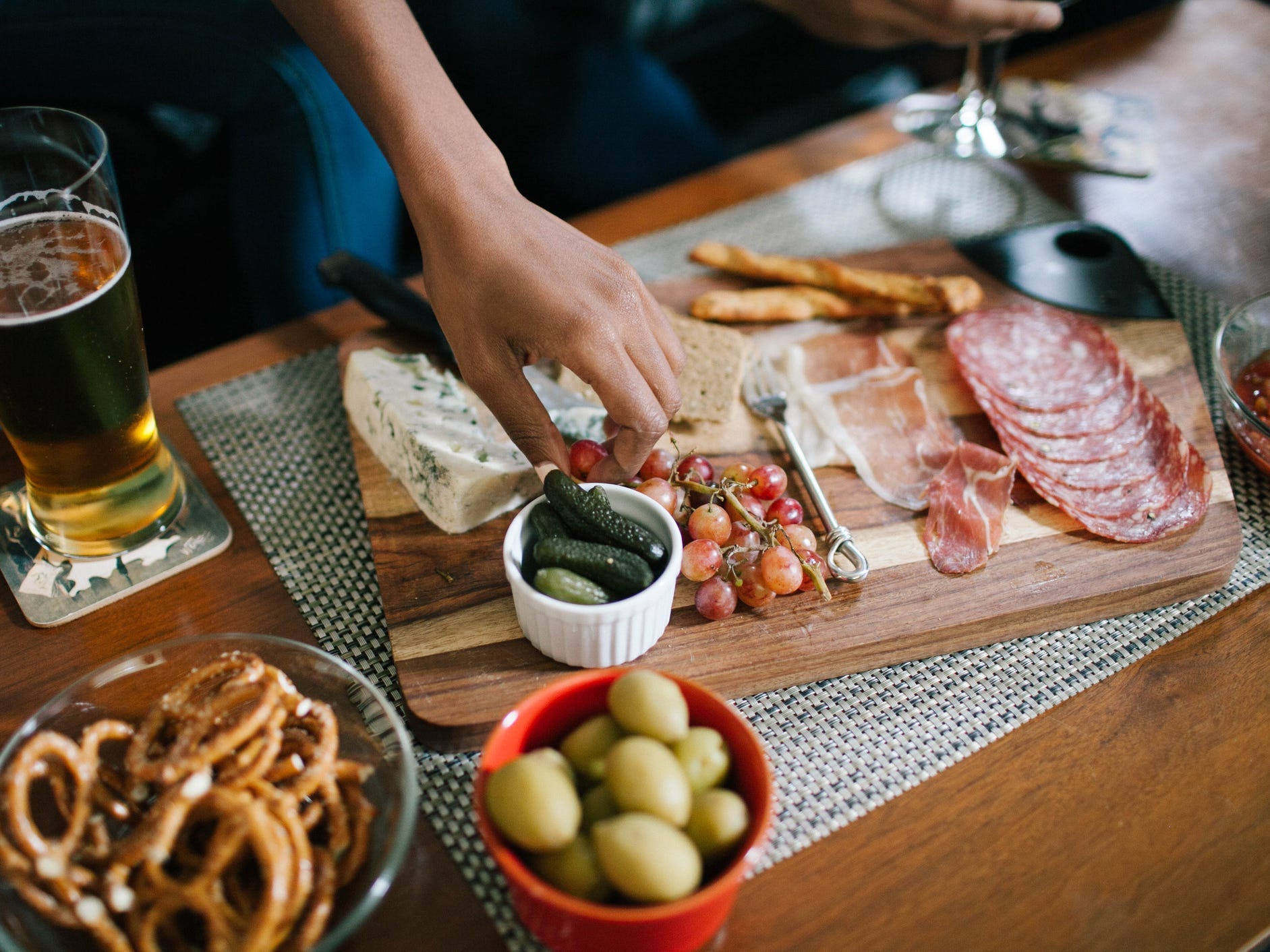 Someone picking a grape off of a charcuterie board.