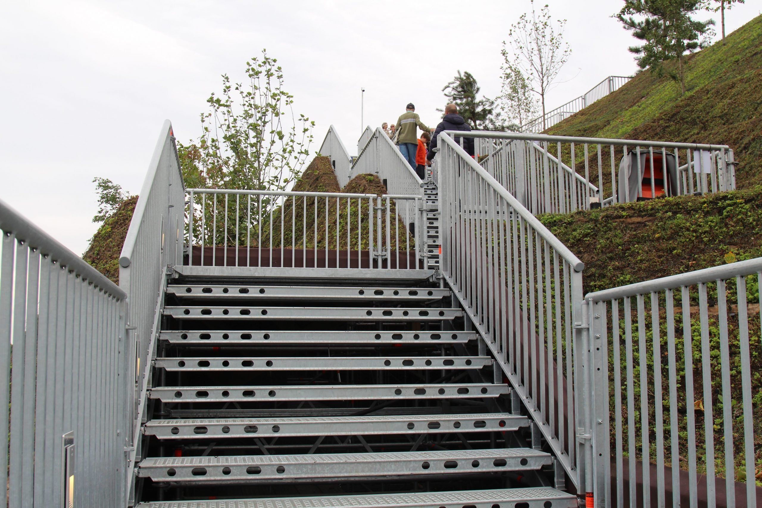 A metal staircase winds its way up an artificial hill in the open air.