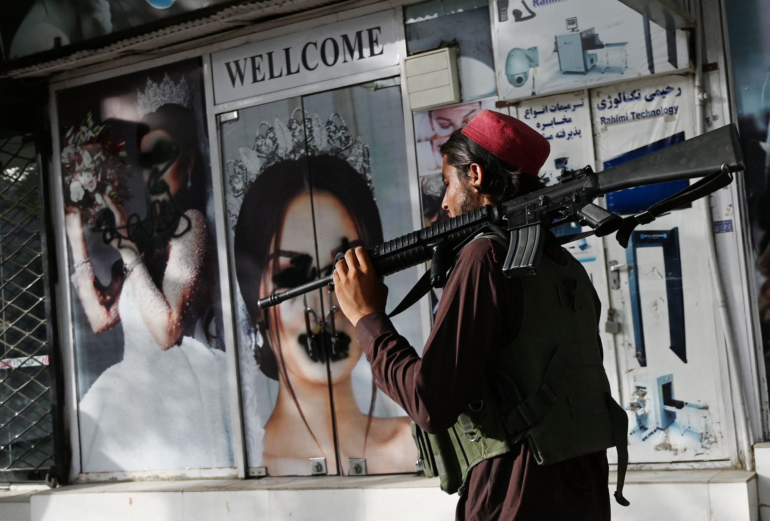 A Taliban fighter walks past a beauty saloon with images of women defaced using a spray paint in Shar-e-Naw in Kabul.