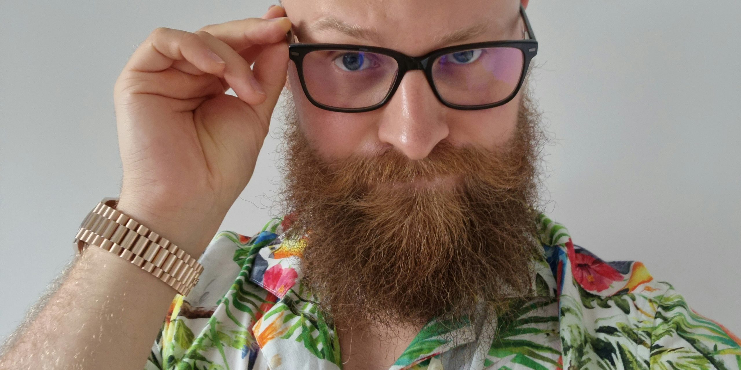 This is a photo of Adrian Zduńczyk in a shirt with parrot prints touching his glasses.