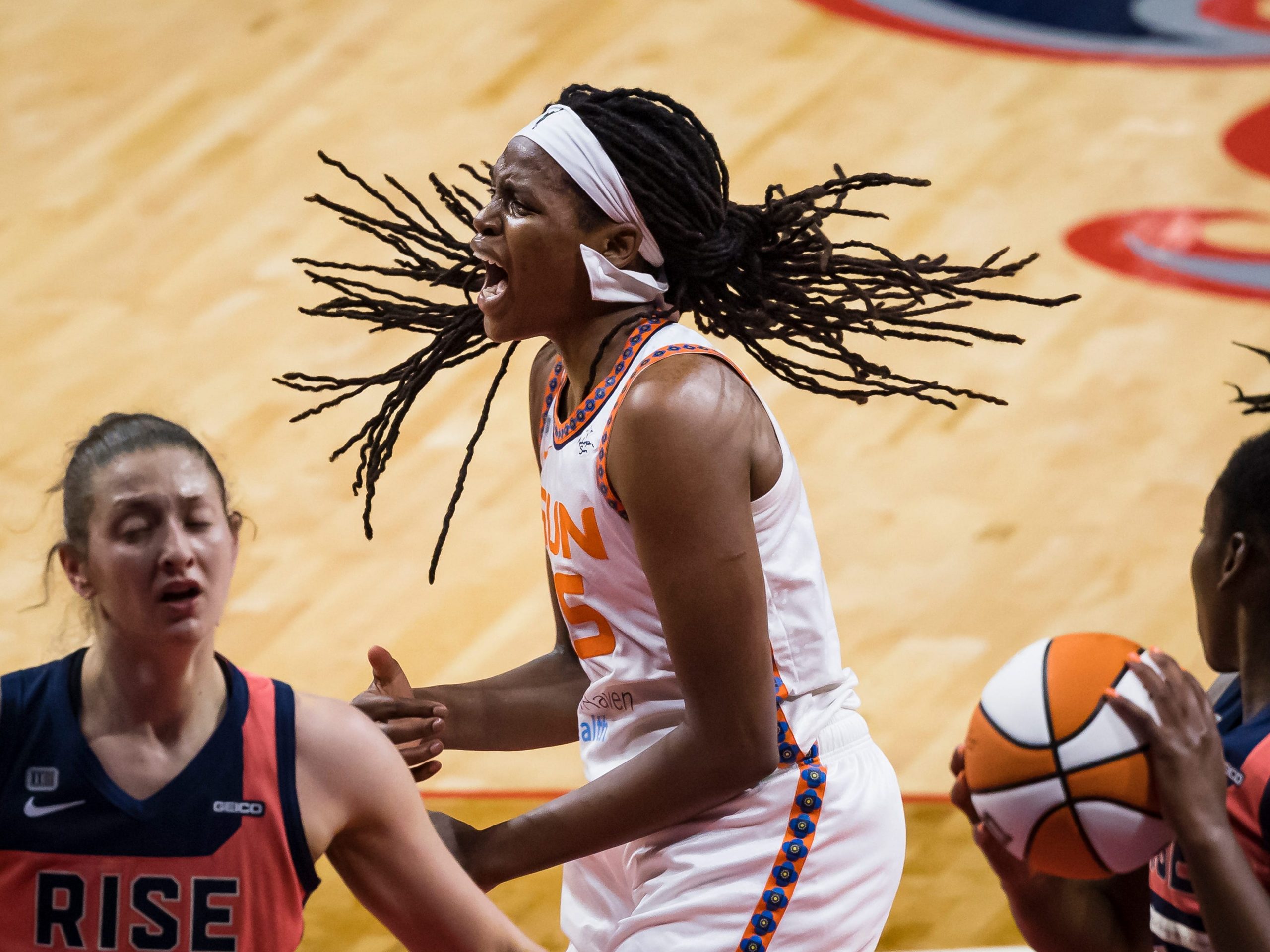 A basketball player stands open-mouthed as players stand to her either side.