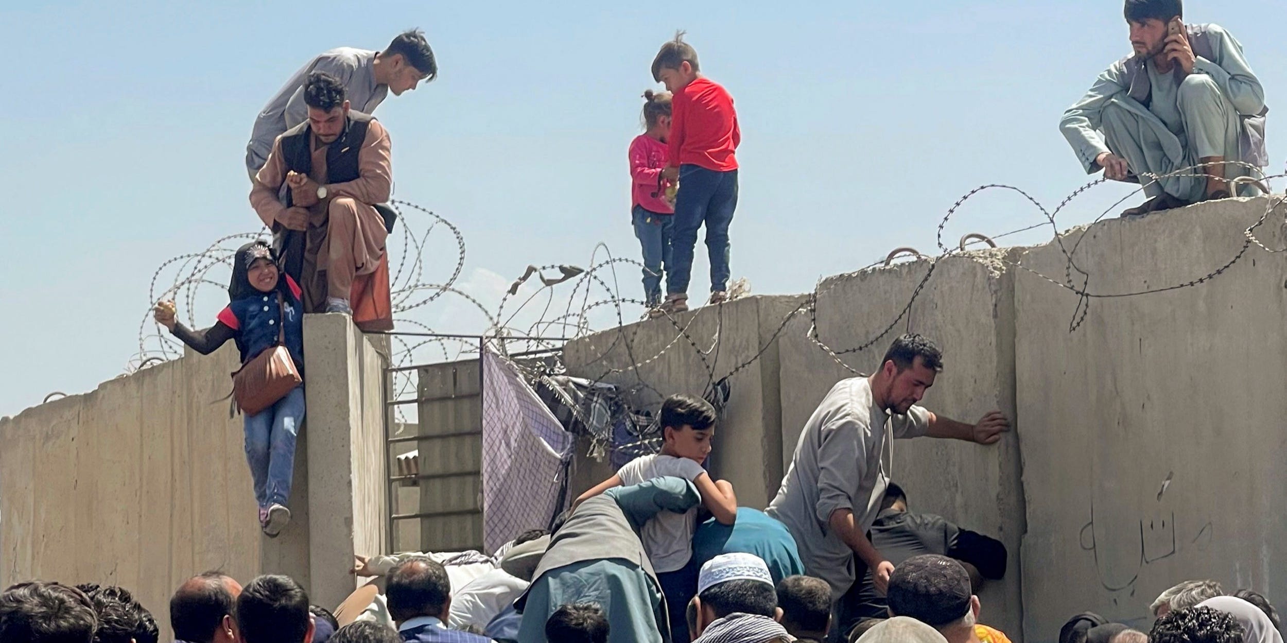 Afghanis climbing over the Kabul Airport fence in Afghanistan