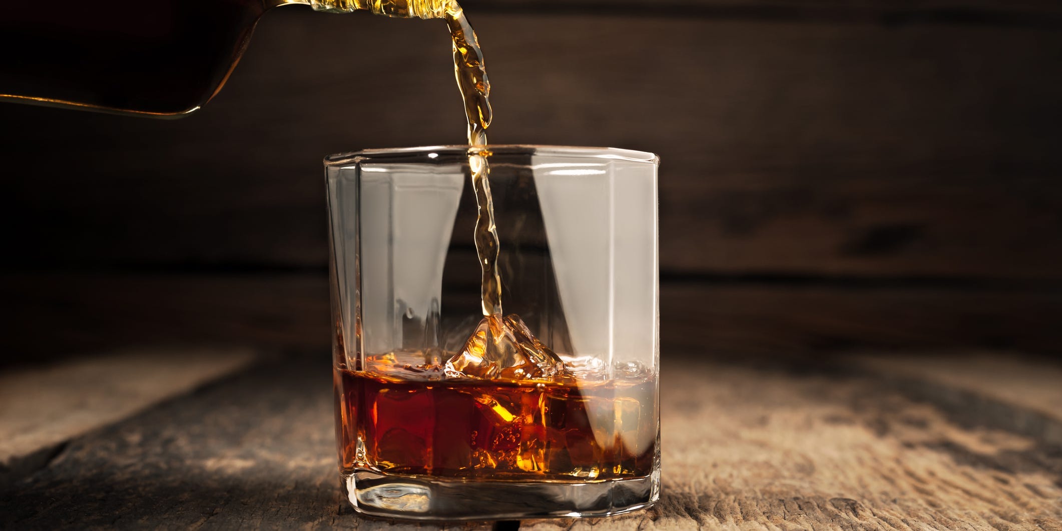 Whiskey being poured over ice into a rocks glass