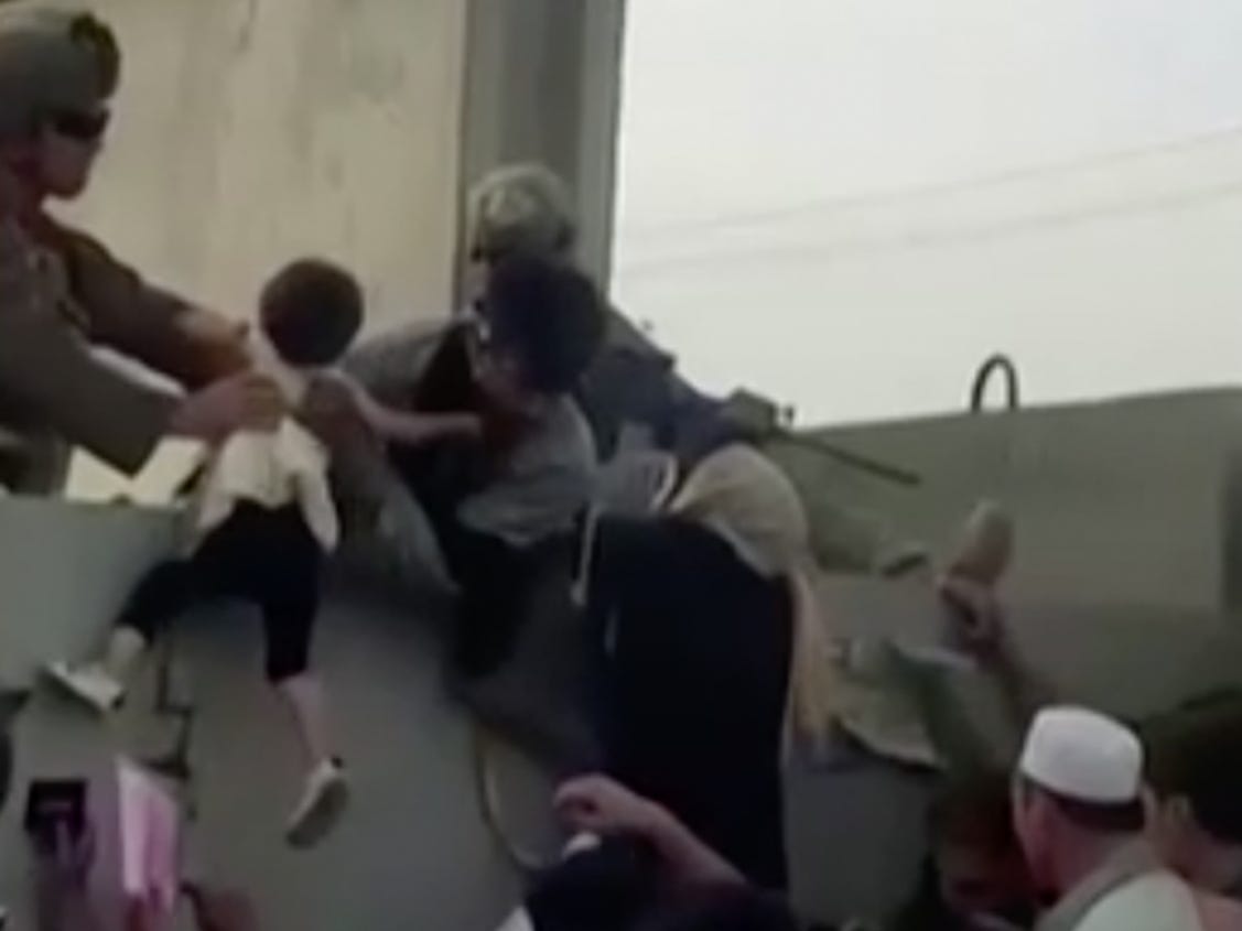 An Afghan girl is pulled over a wall to U.S. forces at Kabul airport.