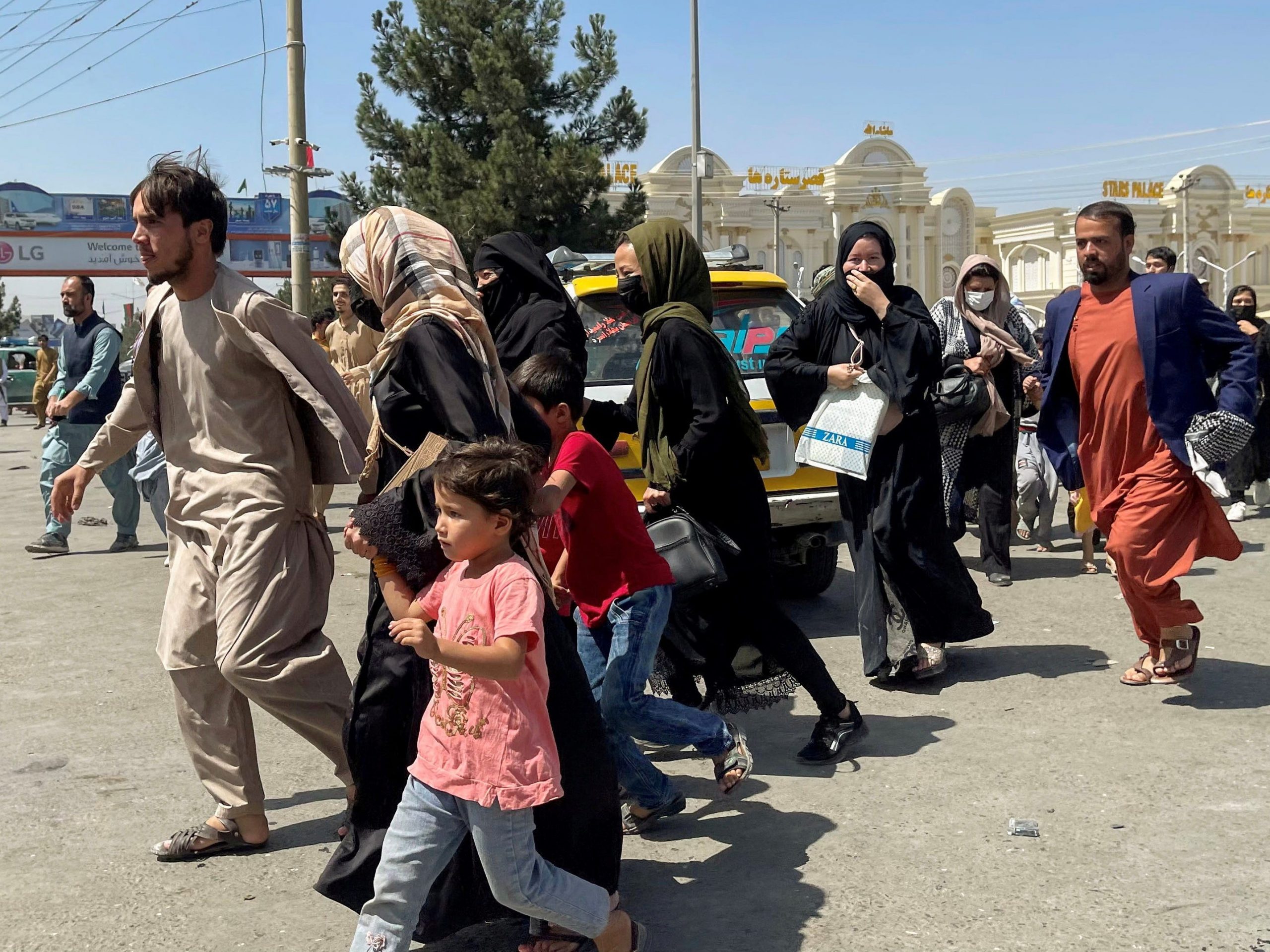 A dozen Afghan people are running, one woman is holding the hand of a child.