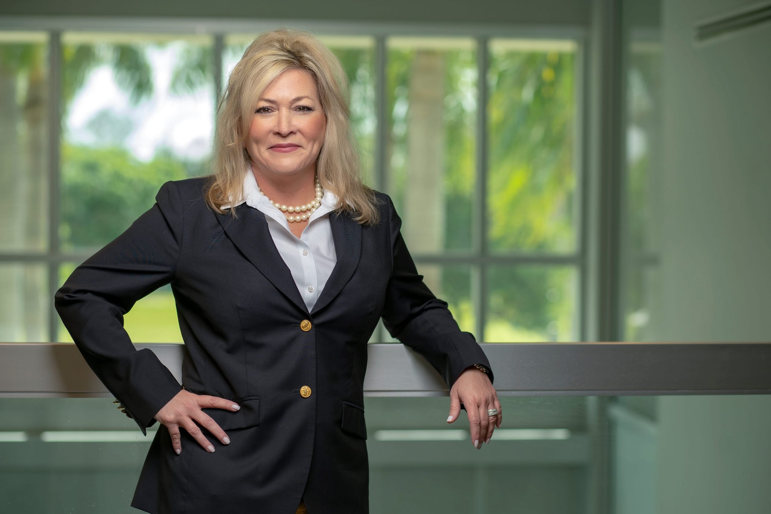 A portrait of Karen Jones, EVP and CMO of Ryder, wearing a suit with a pearl necklace while posing with one hand on her hip and leaning against a railing.