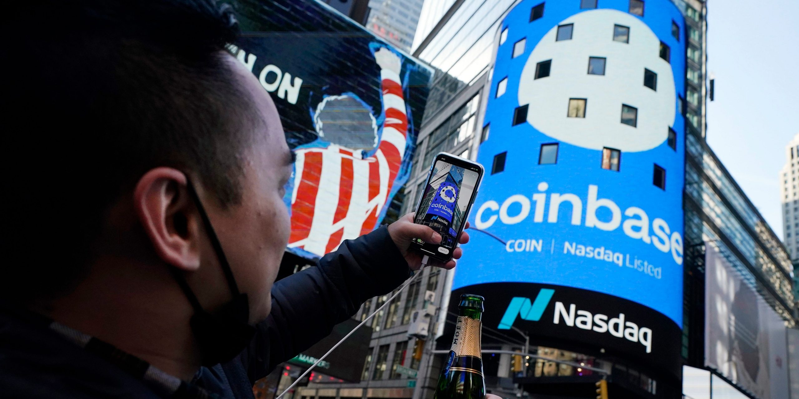 Coinbase employee Daniel Huynh holds a celebratory bottle of champagne as he photographs outside the Nasdaq MarketSite, in New York's Times Square, Wednesday, April 14, 2021.