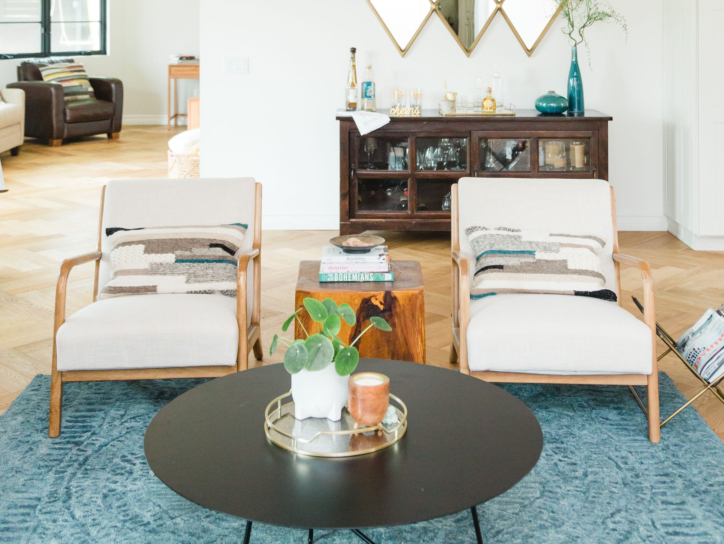 A white living room with wood beams, beige chairs, and a blue carpet.