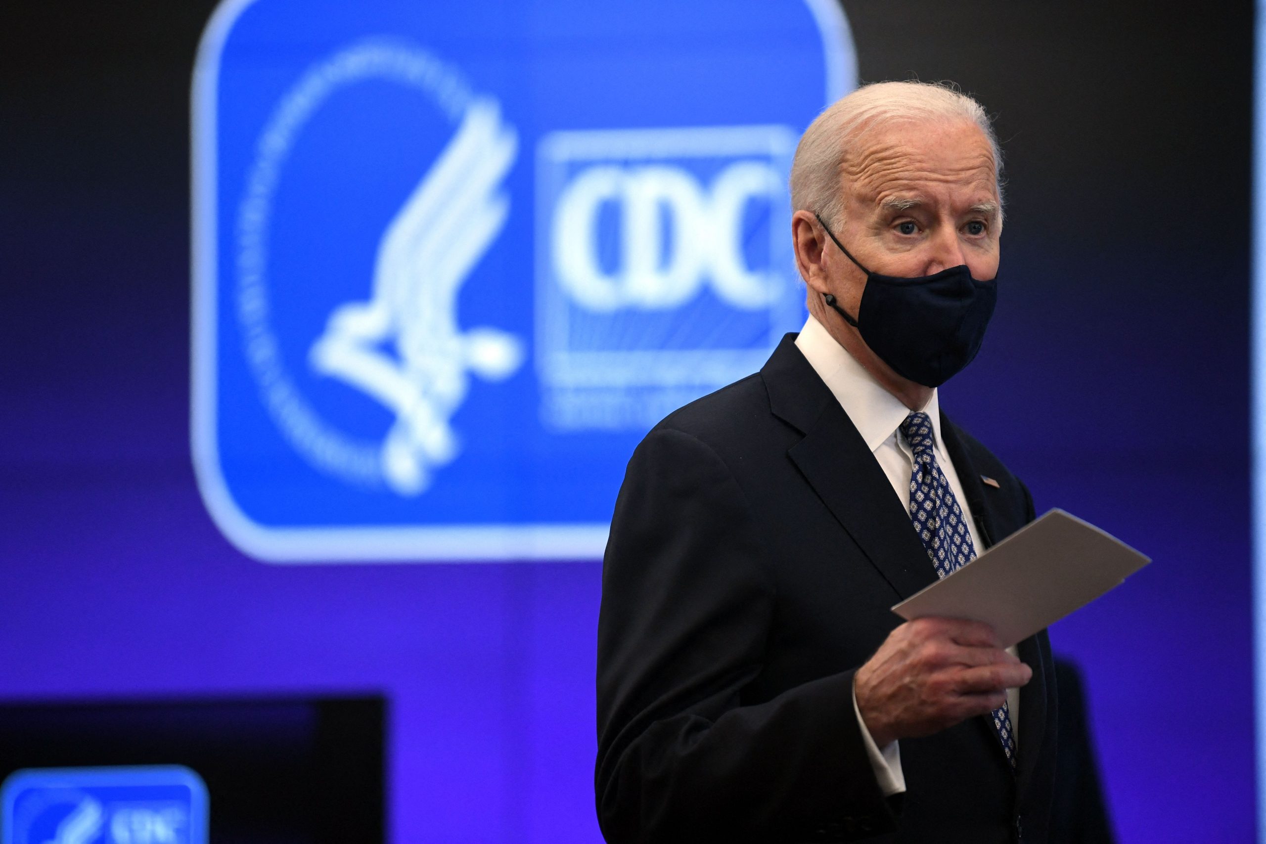 President Joe Biden wears a face mask in front of a blue CDC sign