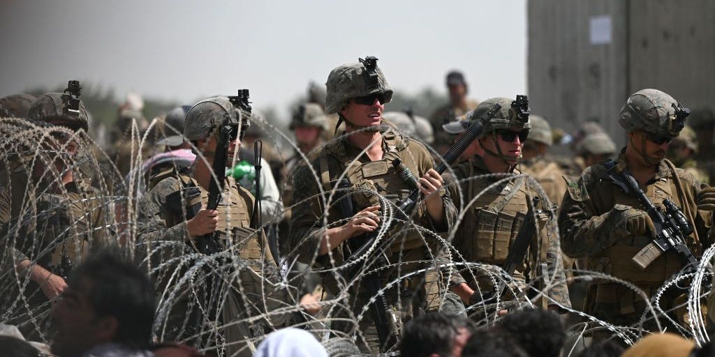 US soldiers stand guard behind barbed wire as Afghans sit on a roadside near the military part of the airport in Kabul on August 20, 2021, hoping to flee from the country after the Taliban's military takeover of Afghanistan