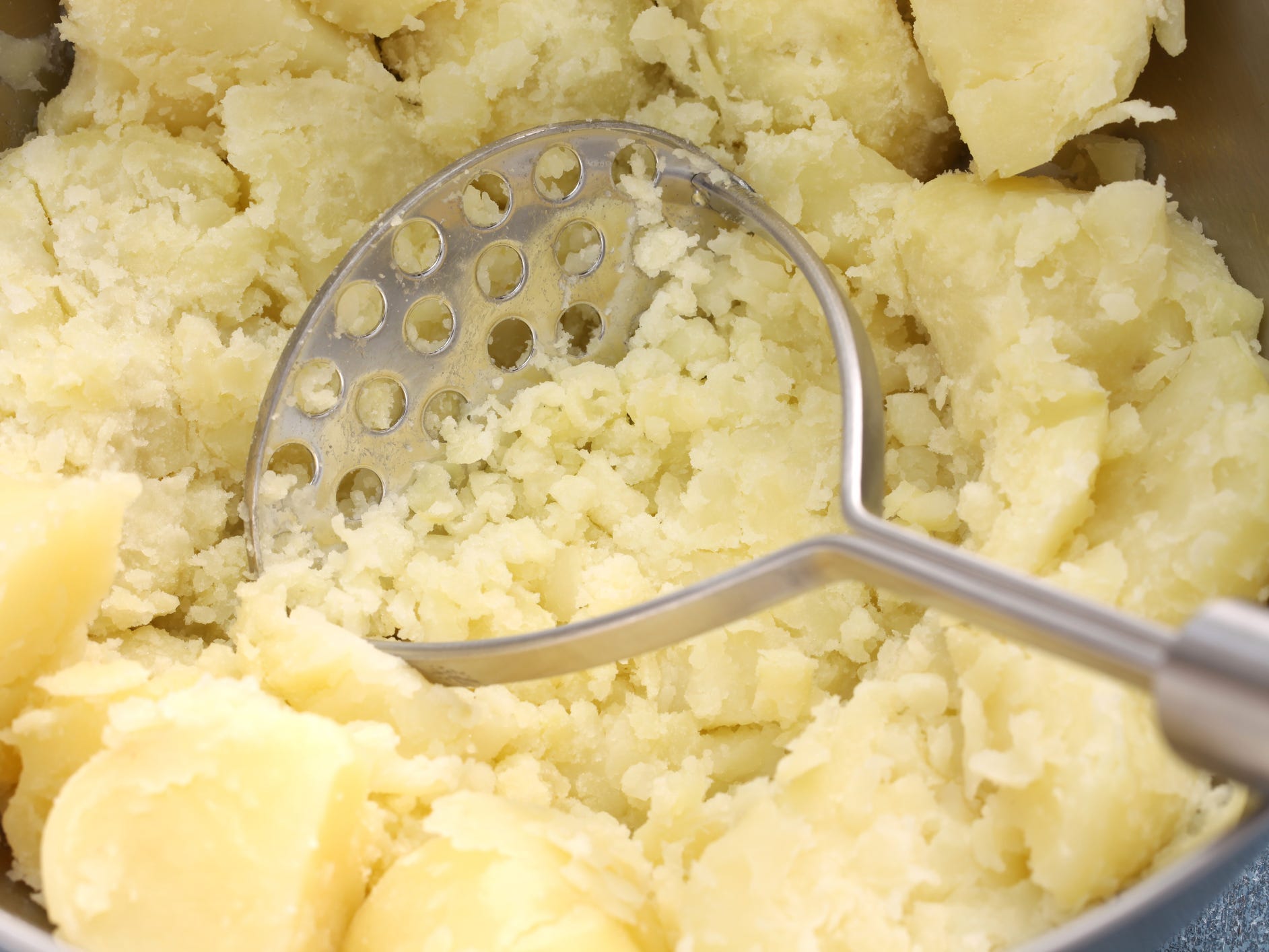 A pot of cooked potatoes being mashed with a potato masher