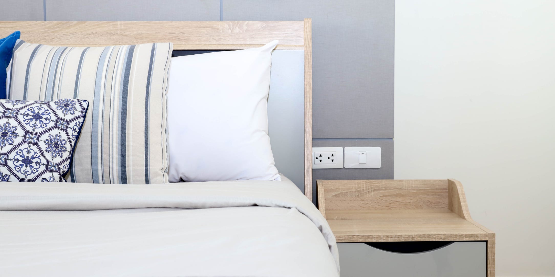 Shot of a bed with white sheets and a wood night stand.