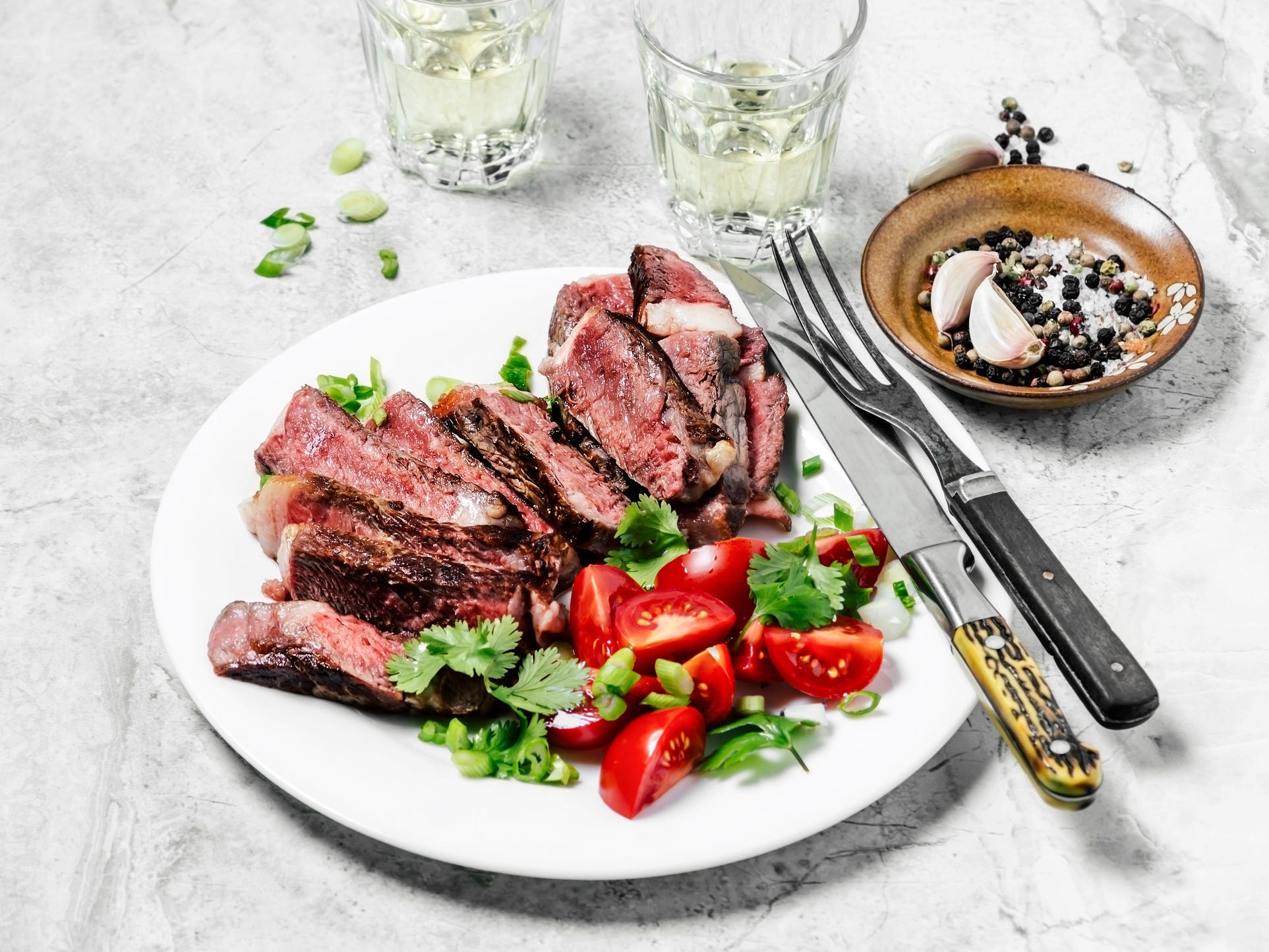 Sliced ribeye steak on a plate with a tomato salad on the side