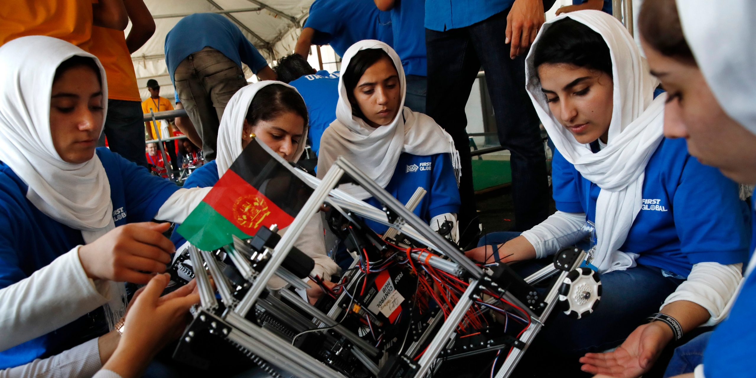 Four Afghan members of a robotics team make repairs on a robot.