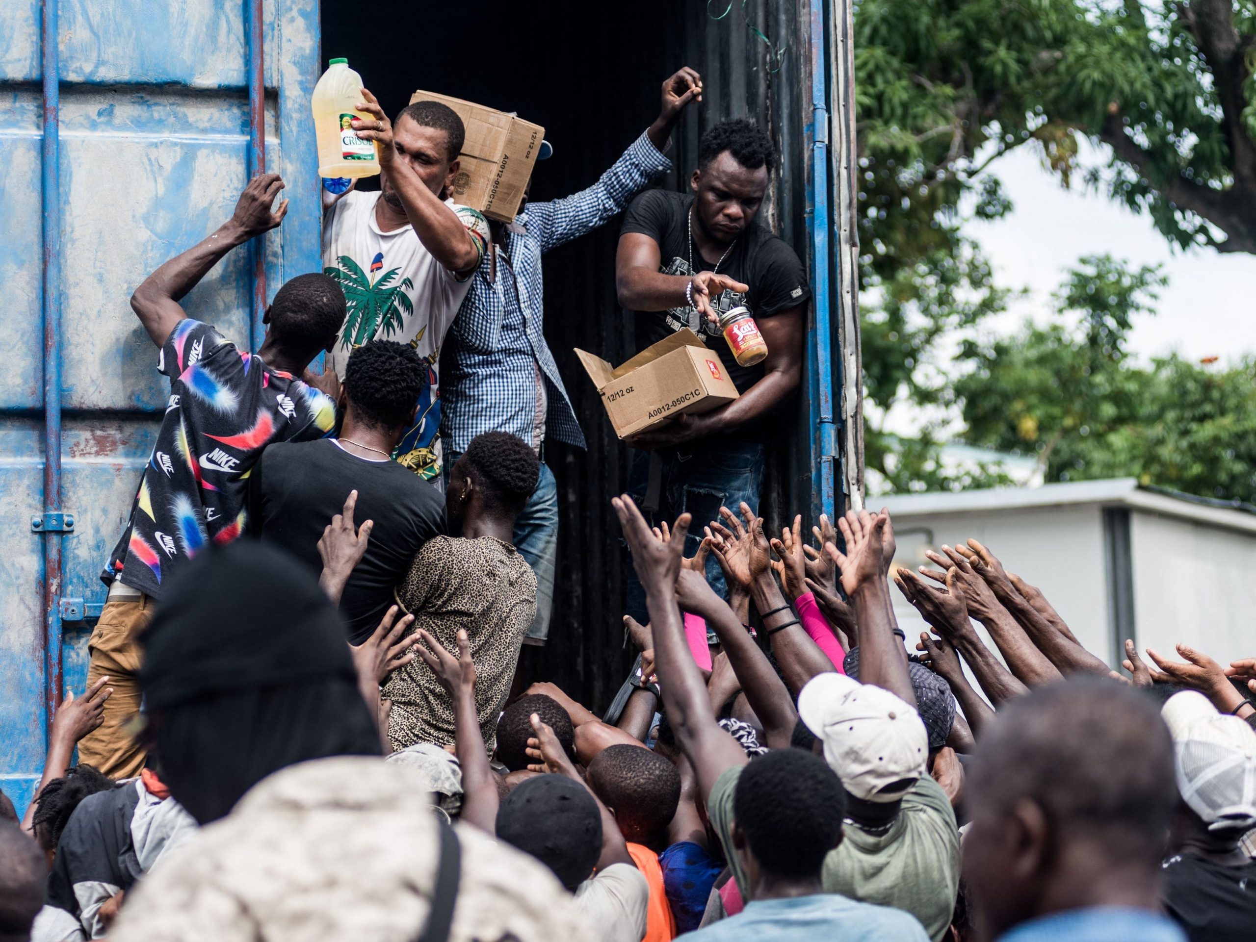 Men hand out supplies to a crowd of earthquake victims during the distribution of food and water at the "4 Chemins" crossroads in Les Cayes, Haiti, August 20, 2021