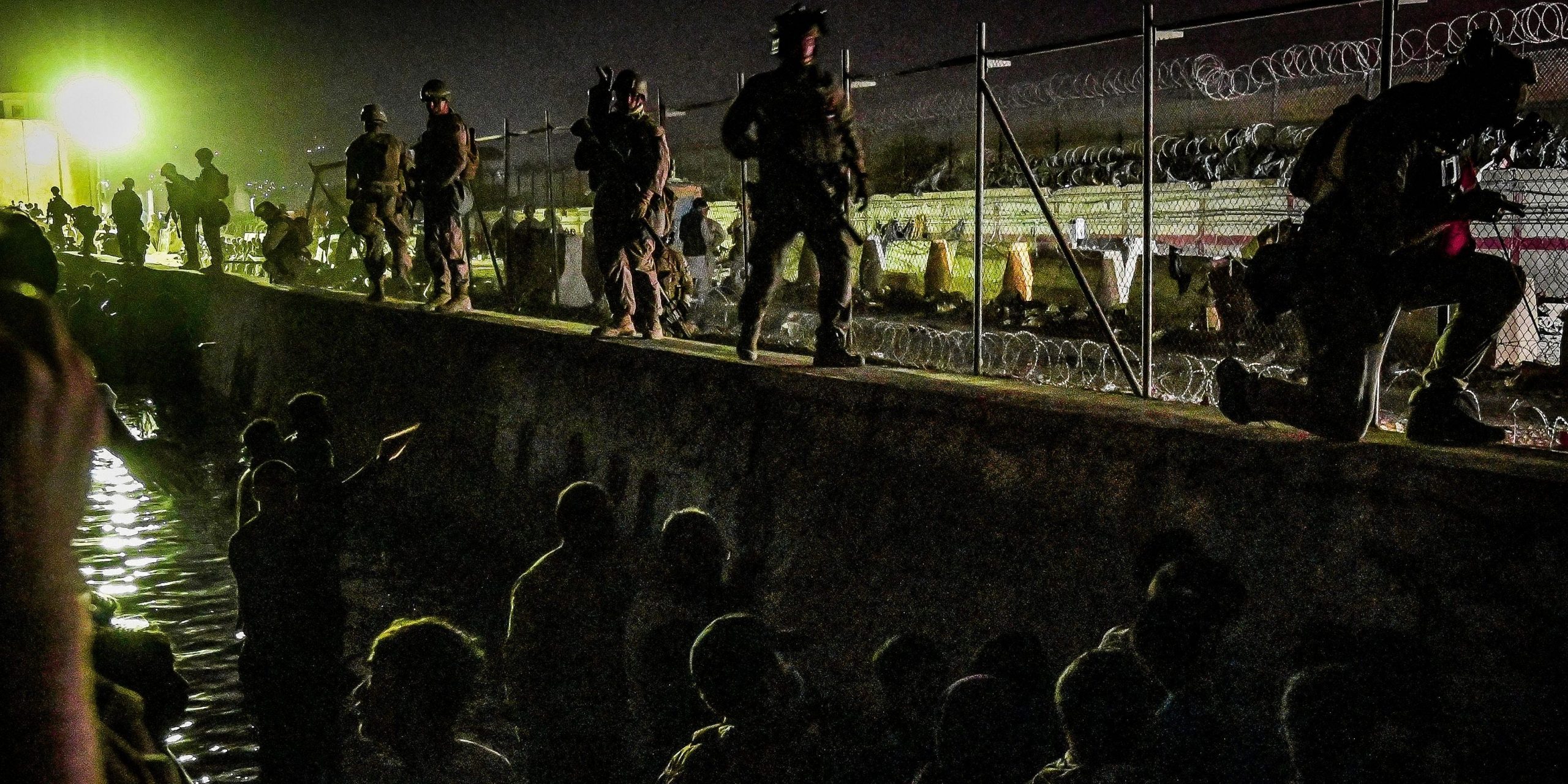 Soldiers stand on a wall at night time while people stand in a canal below them